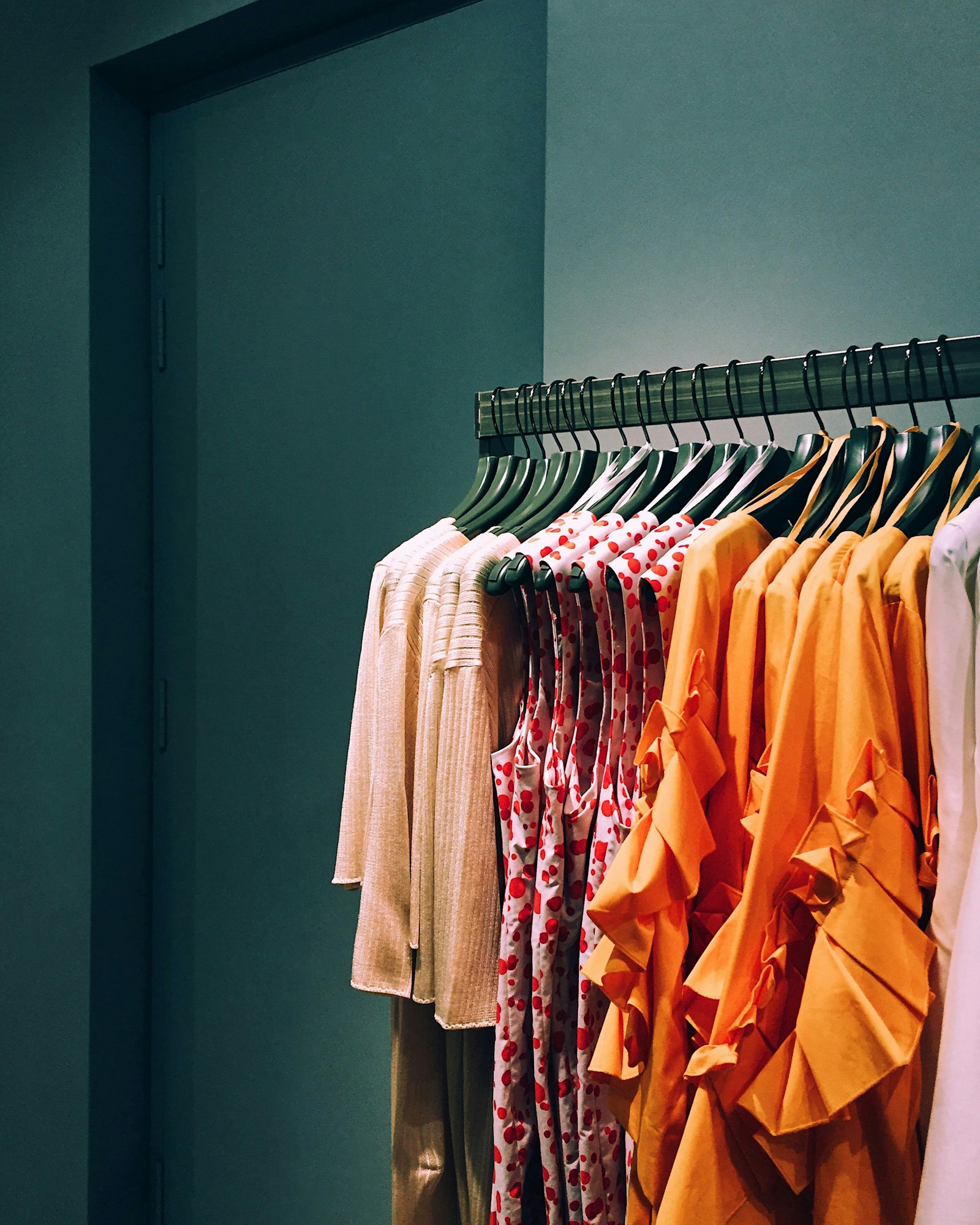 A rack of blank t-shirts and hoodies in assorted colours hanging on wooden hangers in a shop