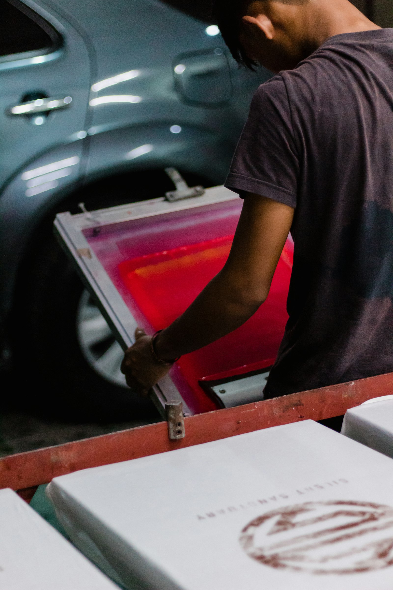 A worker inspecting a printed garment closely under shop lighting, checking the print edge and ink coverage