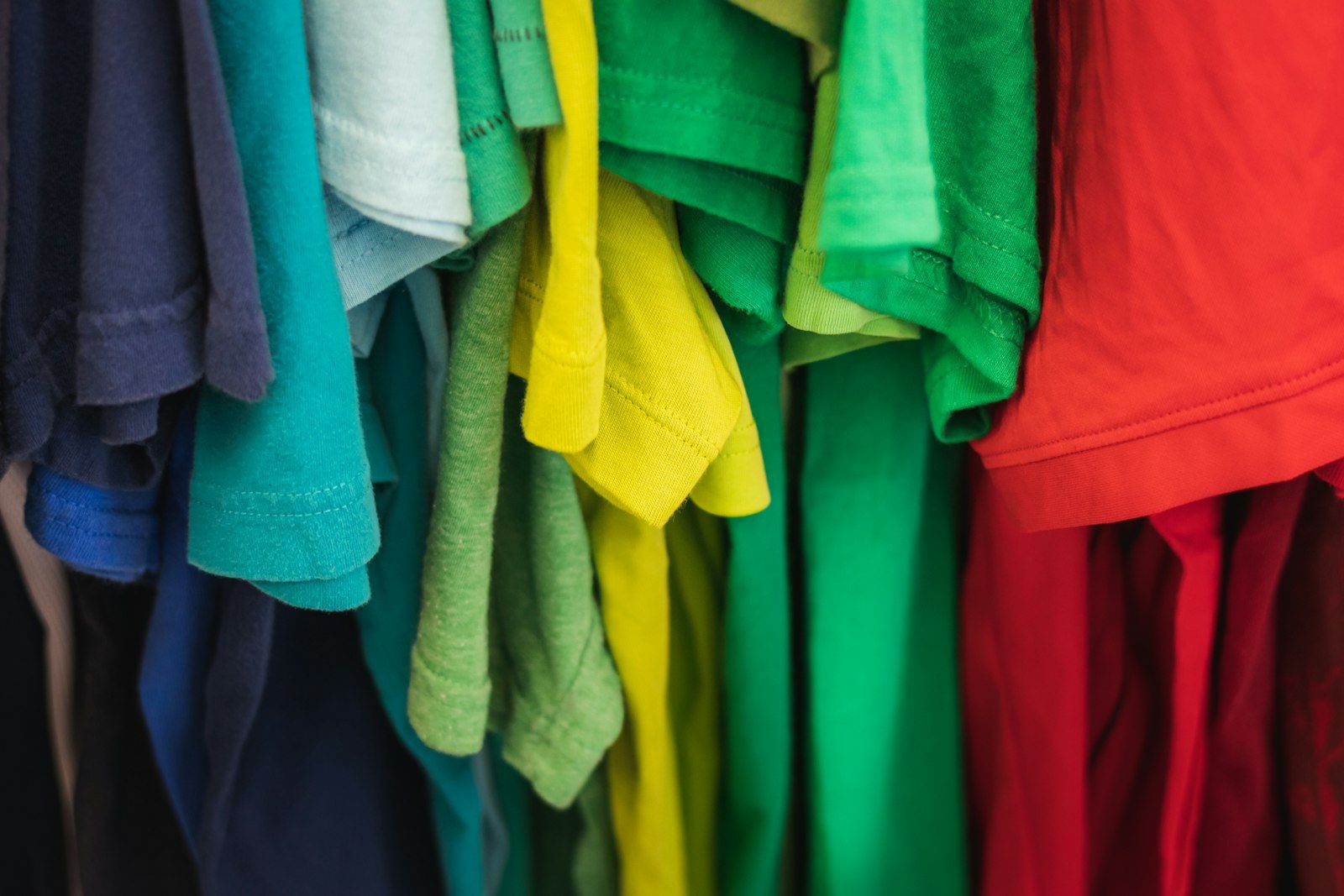 Close-up of t-shirts in navy, teal, green, yellow and red hanging tightly on a rail