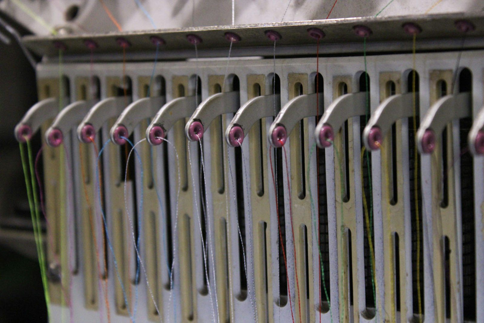 Close-up of the thread guides on a multi-needle embroidery machine, each needle threaded in a different colour