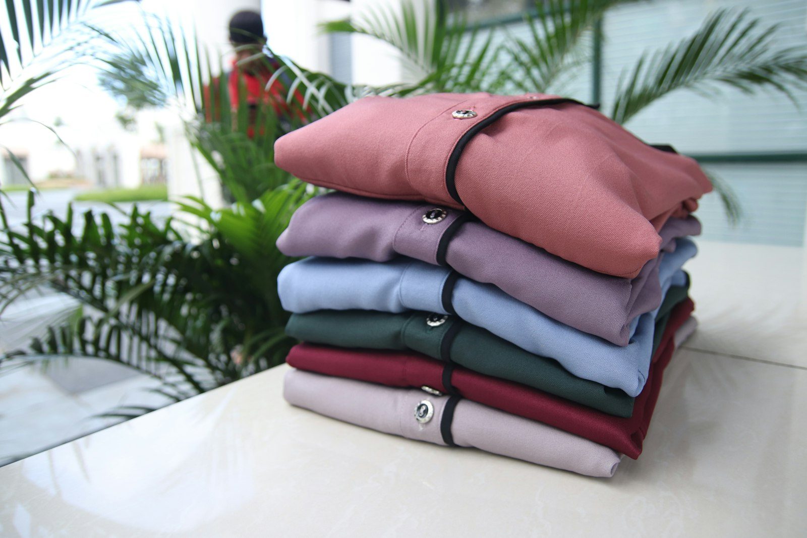 A stack of folded pullover hoodies in pink, lilac, pale blue, green and maroon, drawcords showing, on a white table