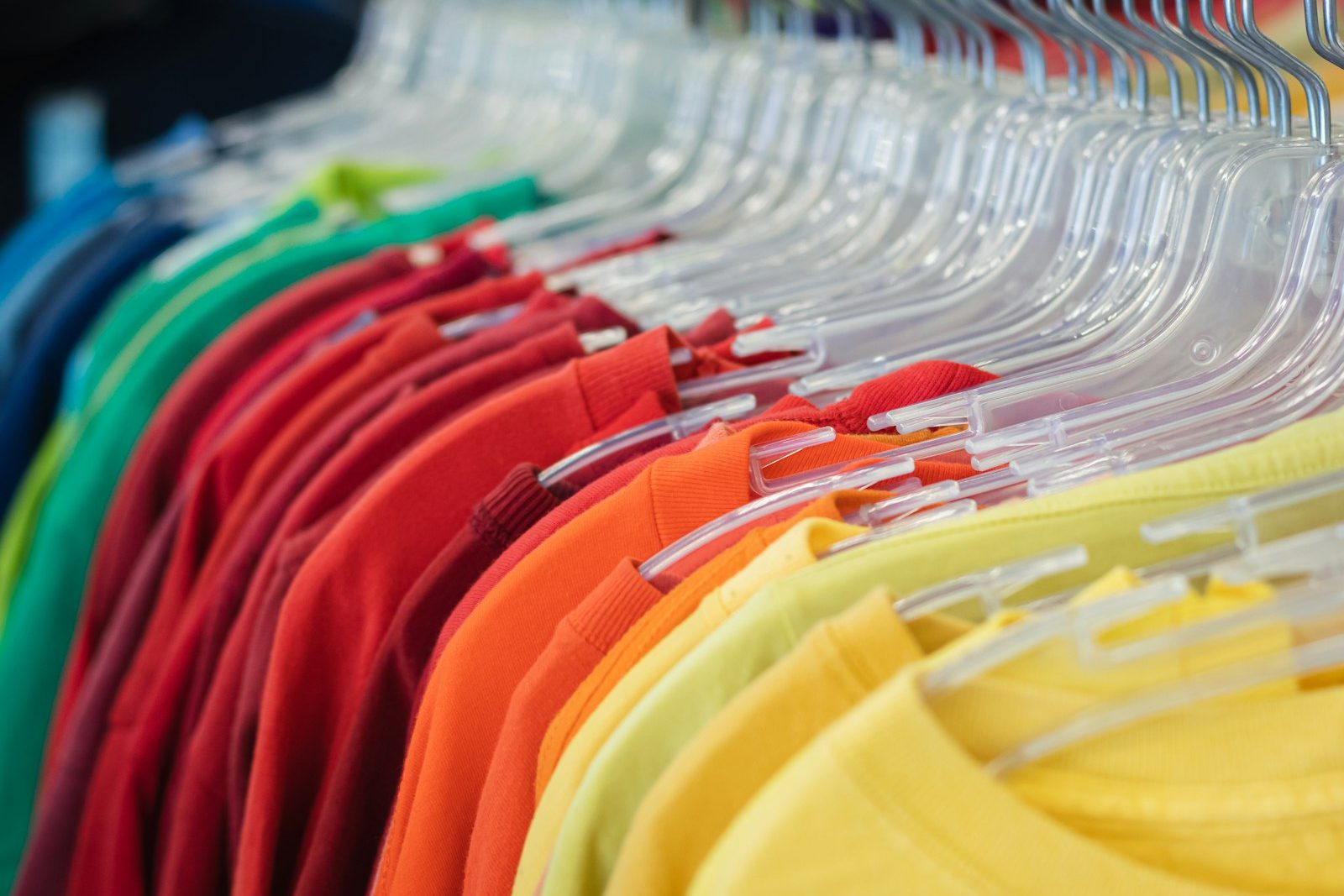 T-shirts on clear plastic hangers in a run of colours from teal and green through red and orange to yellow
