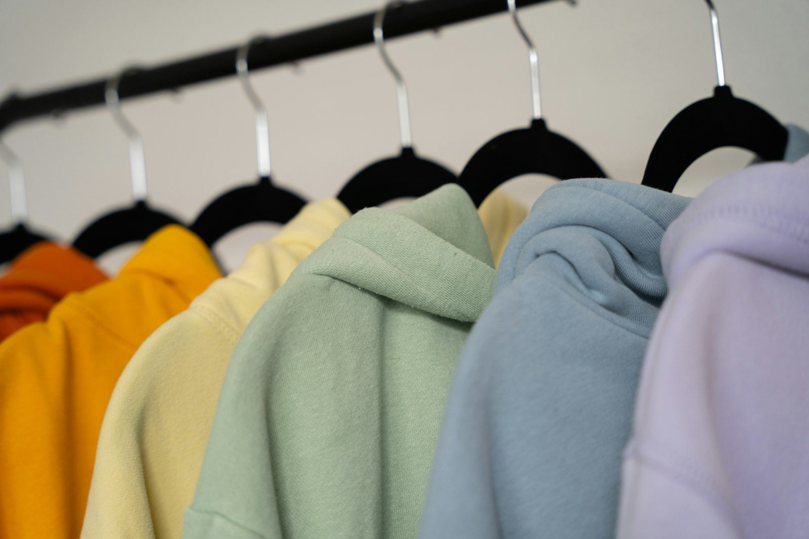 Pullover hoodies in mustard, butter yellow, sage, pale blue and lilac hanging on black velvet hangers