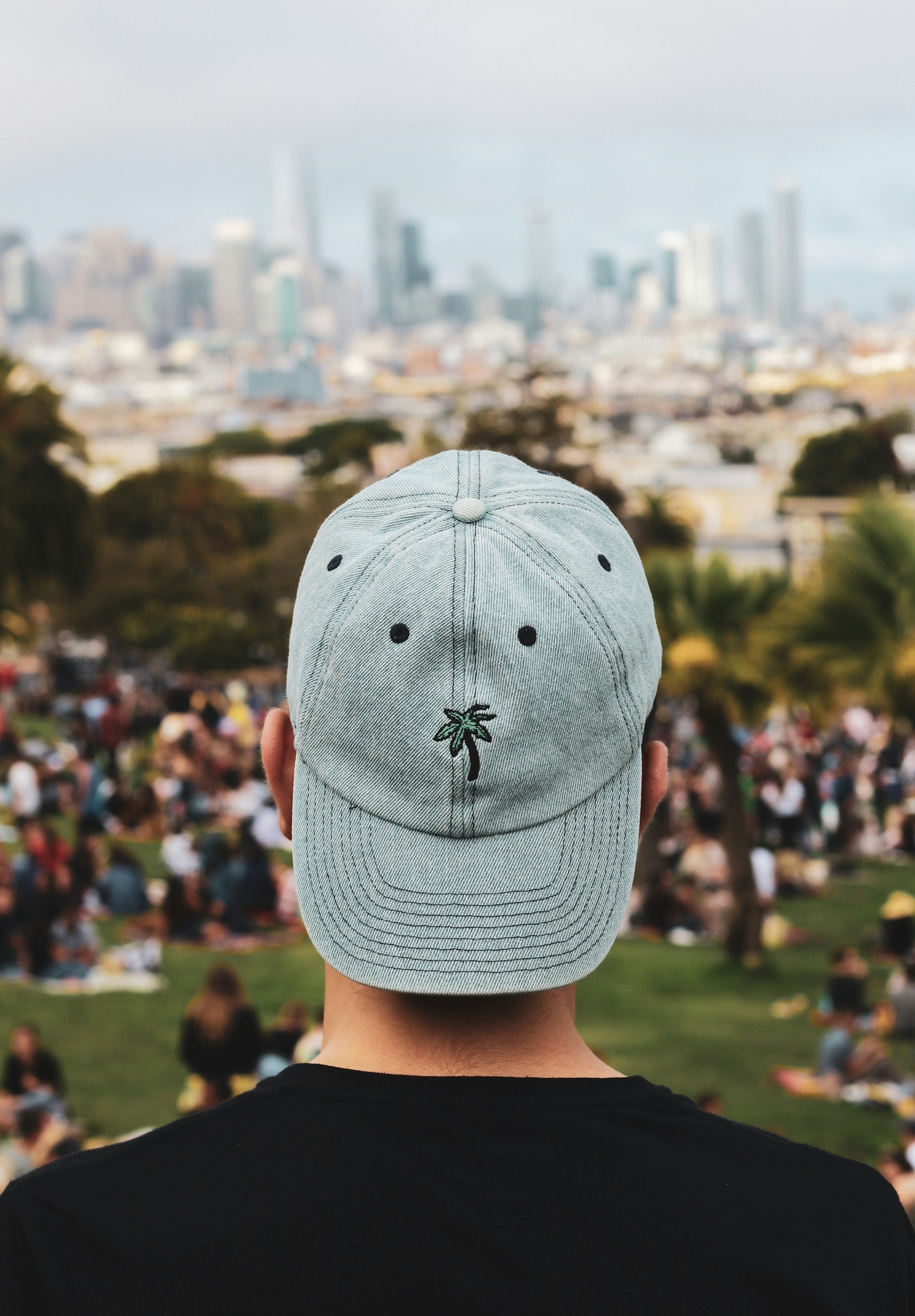 A person seen from behind wearing a pale curved-brim cap with a small embroidered logo, city skyline ahead