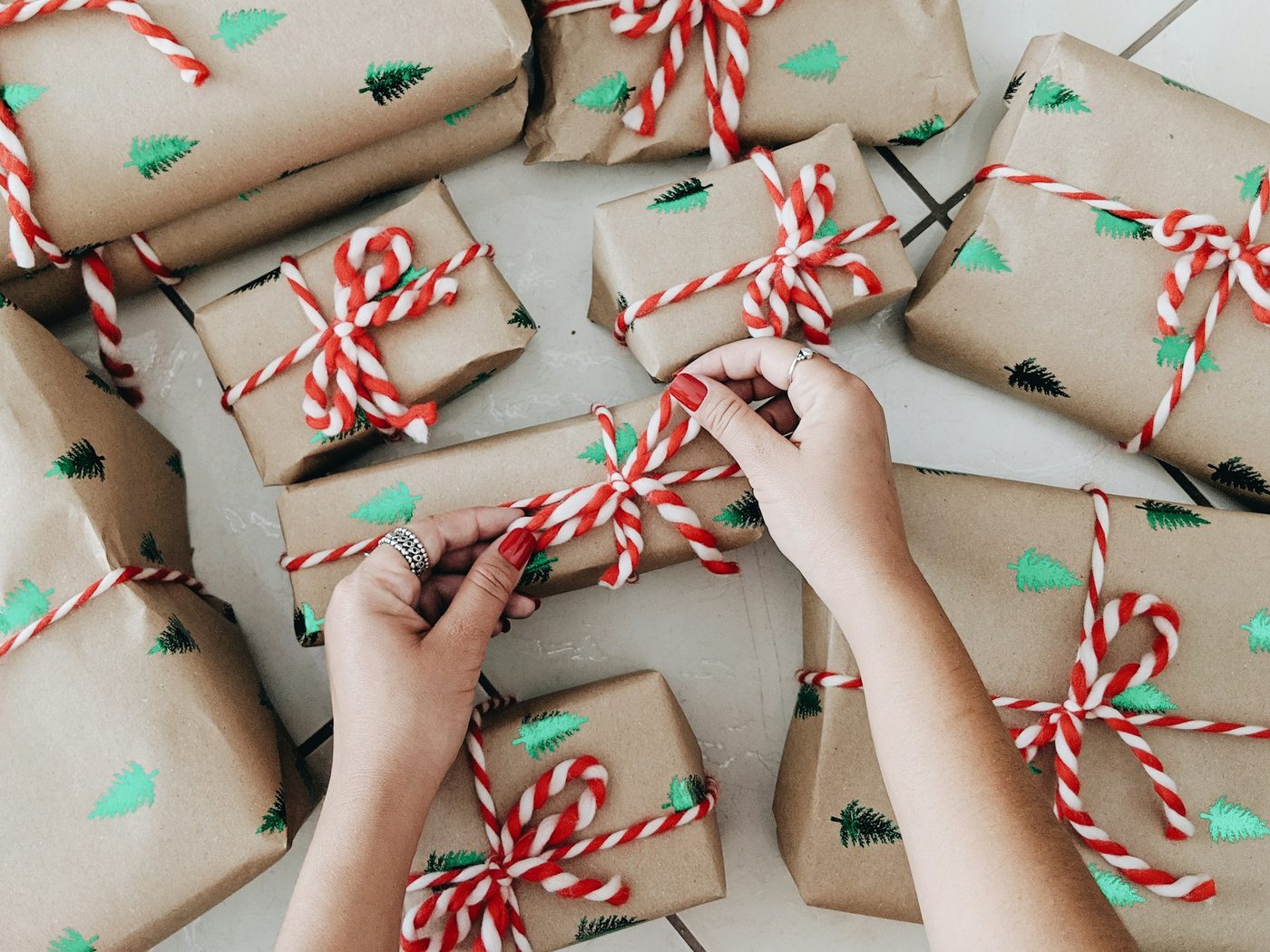 Overhead view of hands tying red-and-white twine bows on kraft-paper parcels stamped with green pine trees