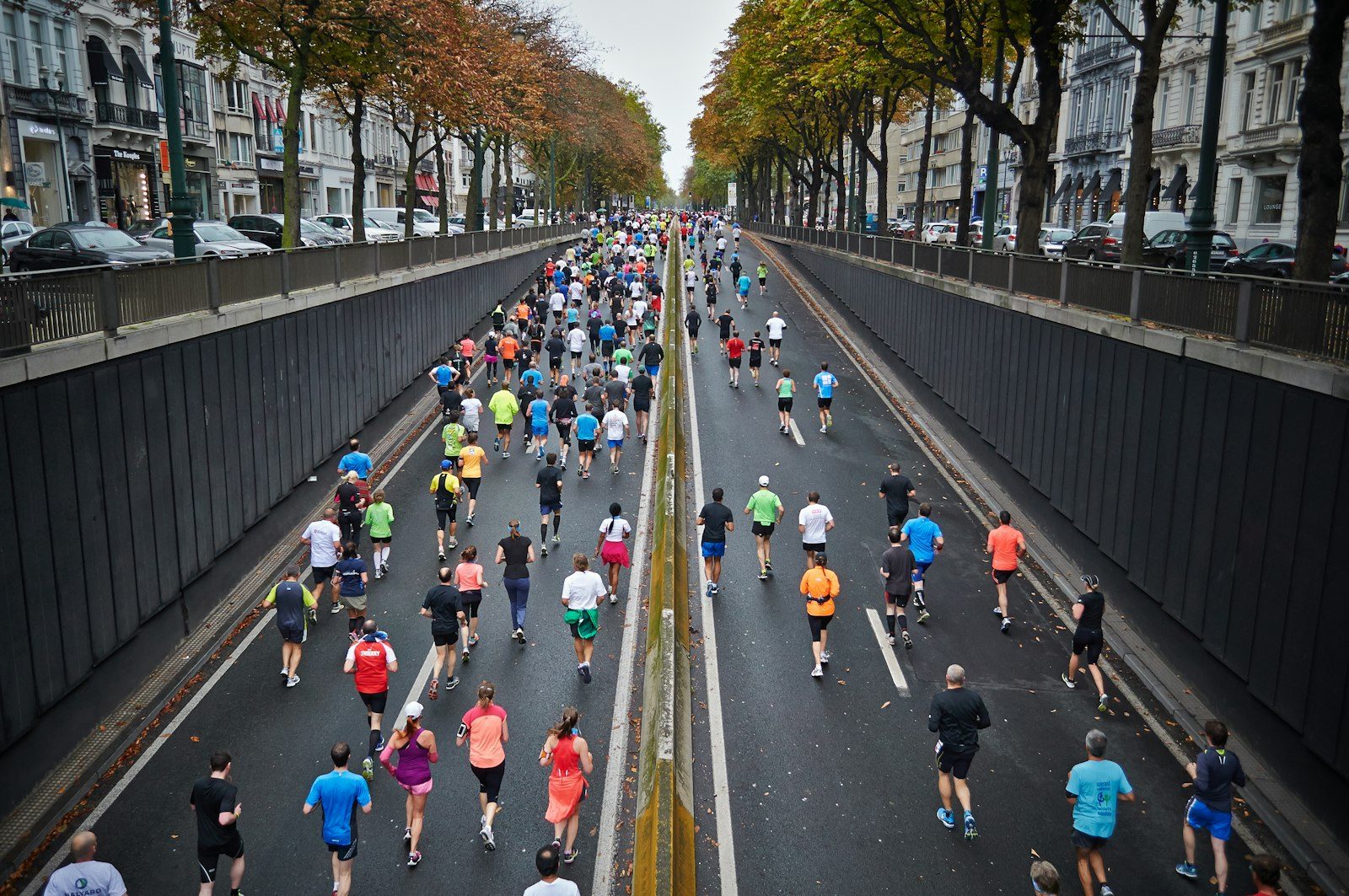 A wide tree-lined avenue filled with hundreds of runners in bright shirts, seen from a bridge above
