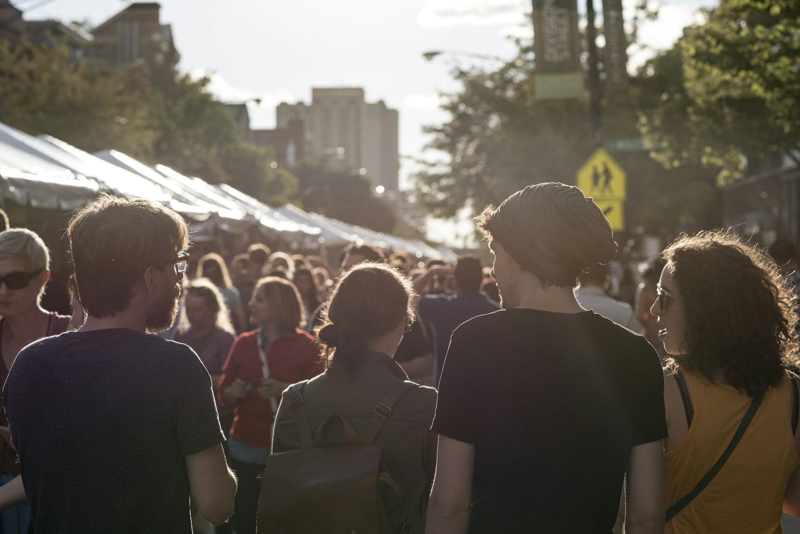 A crowd walking between rows of white vendor tents at a street festival in low evening sunlight