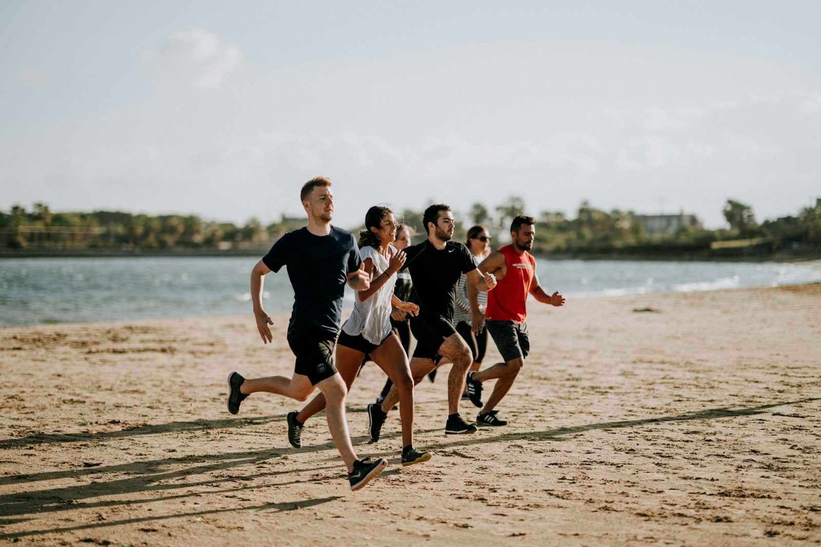 Four runners in black and red t-shirts running along a sandy beach with the lake behind them