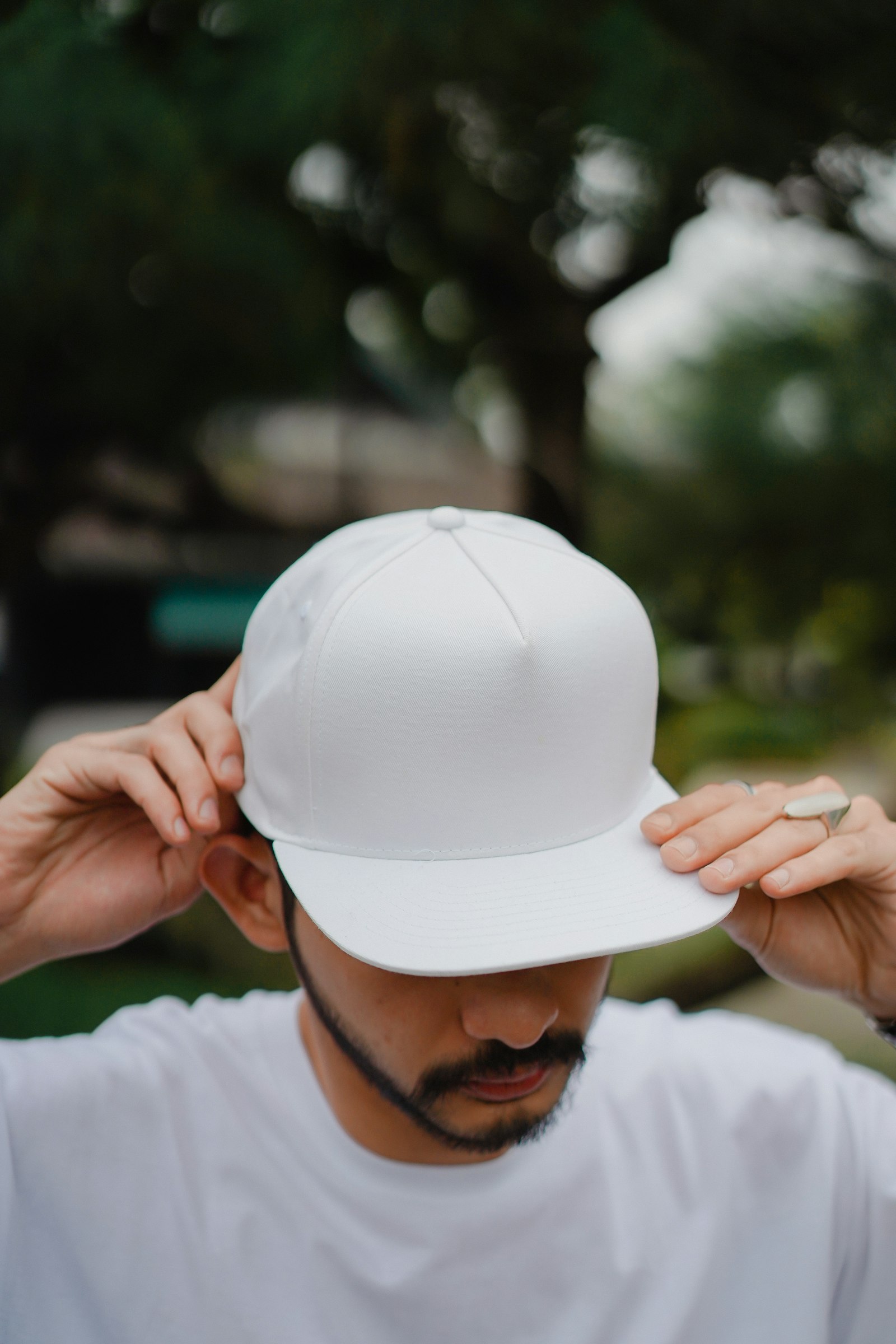 A person holding a plain white flat-brim cap up in both hands outdoors