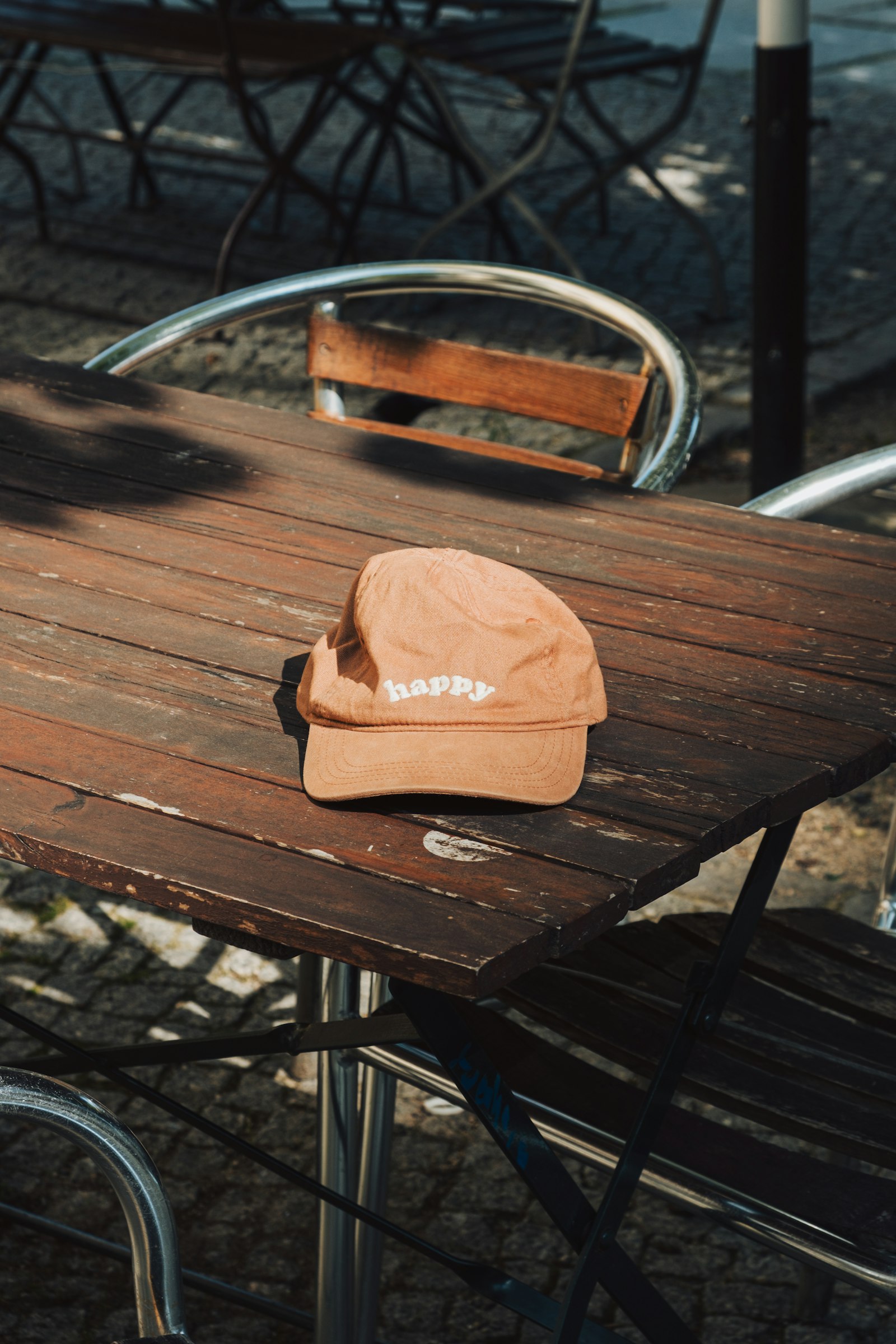 A peach-coloured cap with a small embroidered word on the front, resting on a wooden patio table