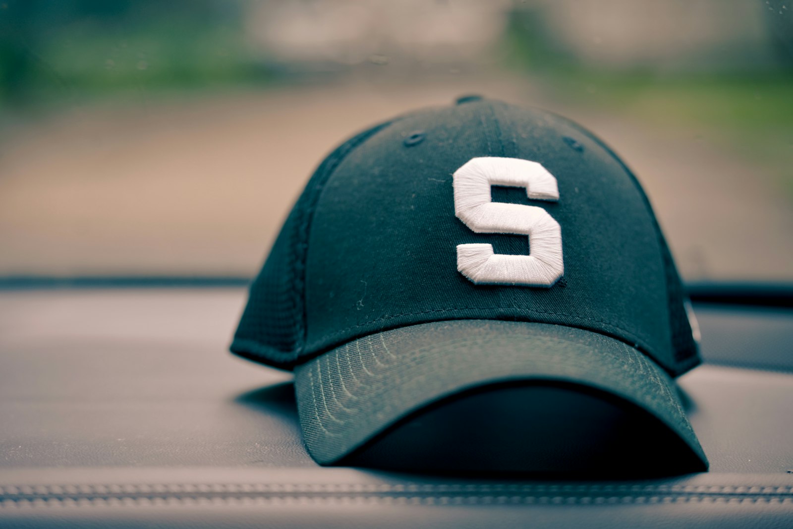 A dark green cap with a large white embroidered letter S centred on the front panel