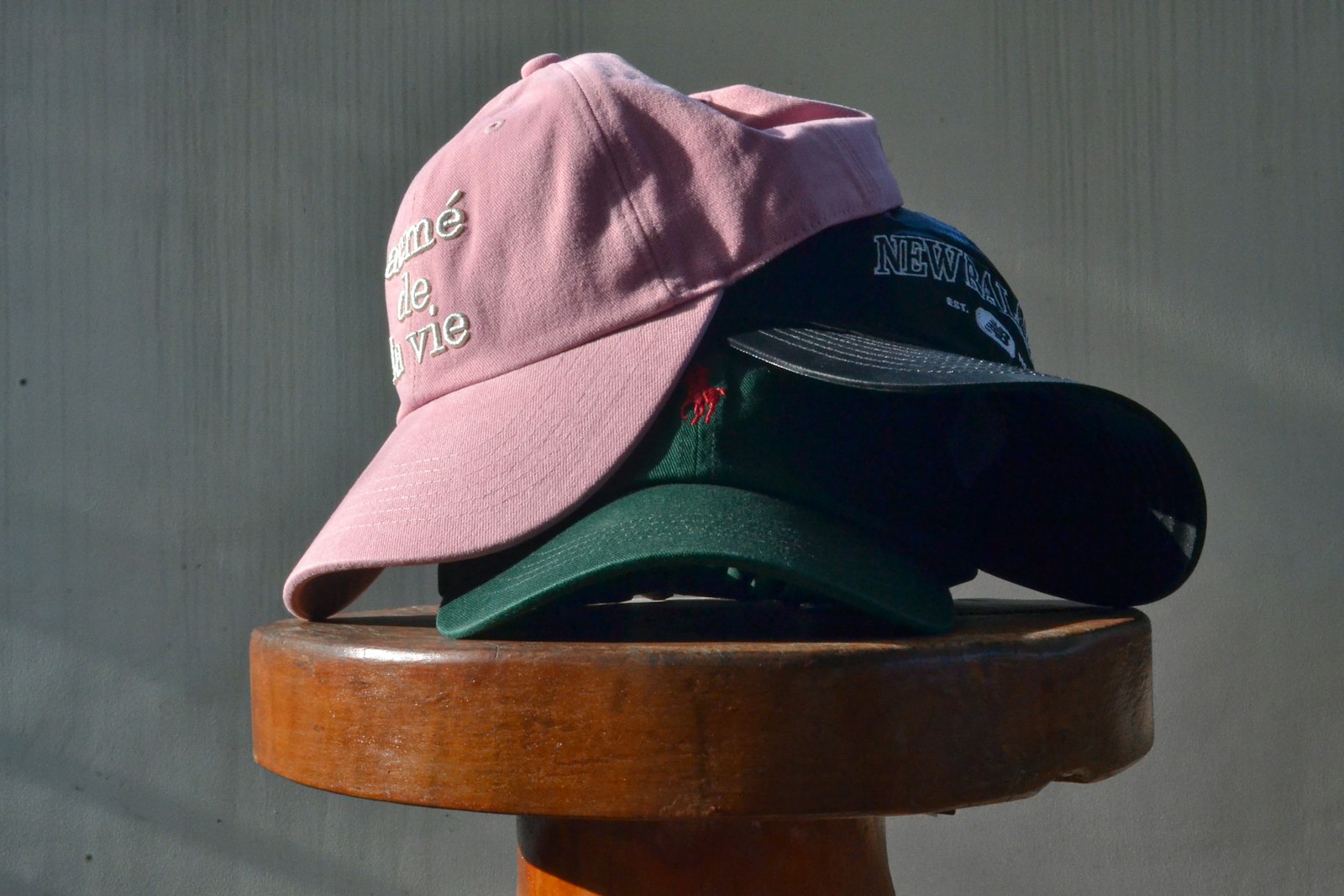 Three custom baseball caps in pink, teal and navy stacked on a wooden stool