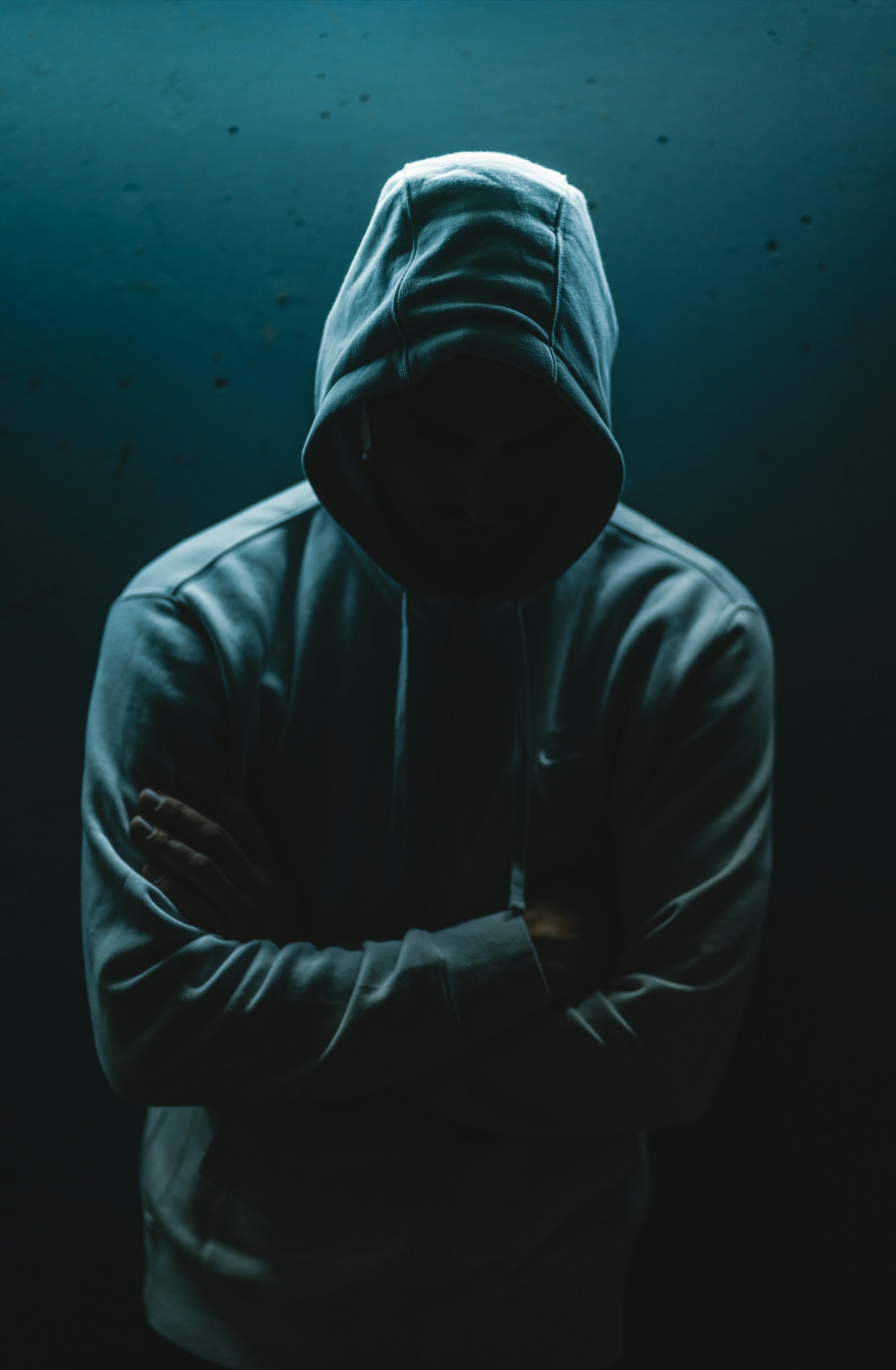 A person in a plain black hooded sweatshirt in low light