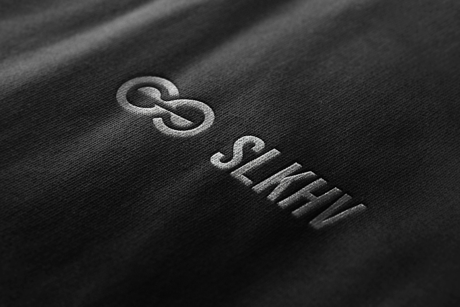Close view of a small pale logo printed on the chest of a dark charcoal garment