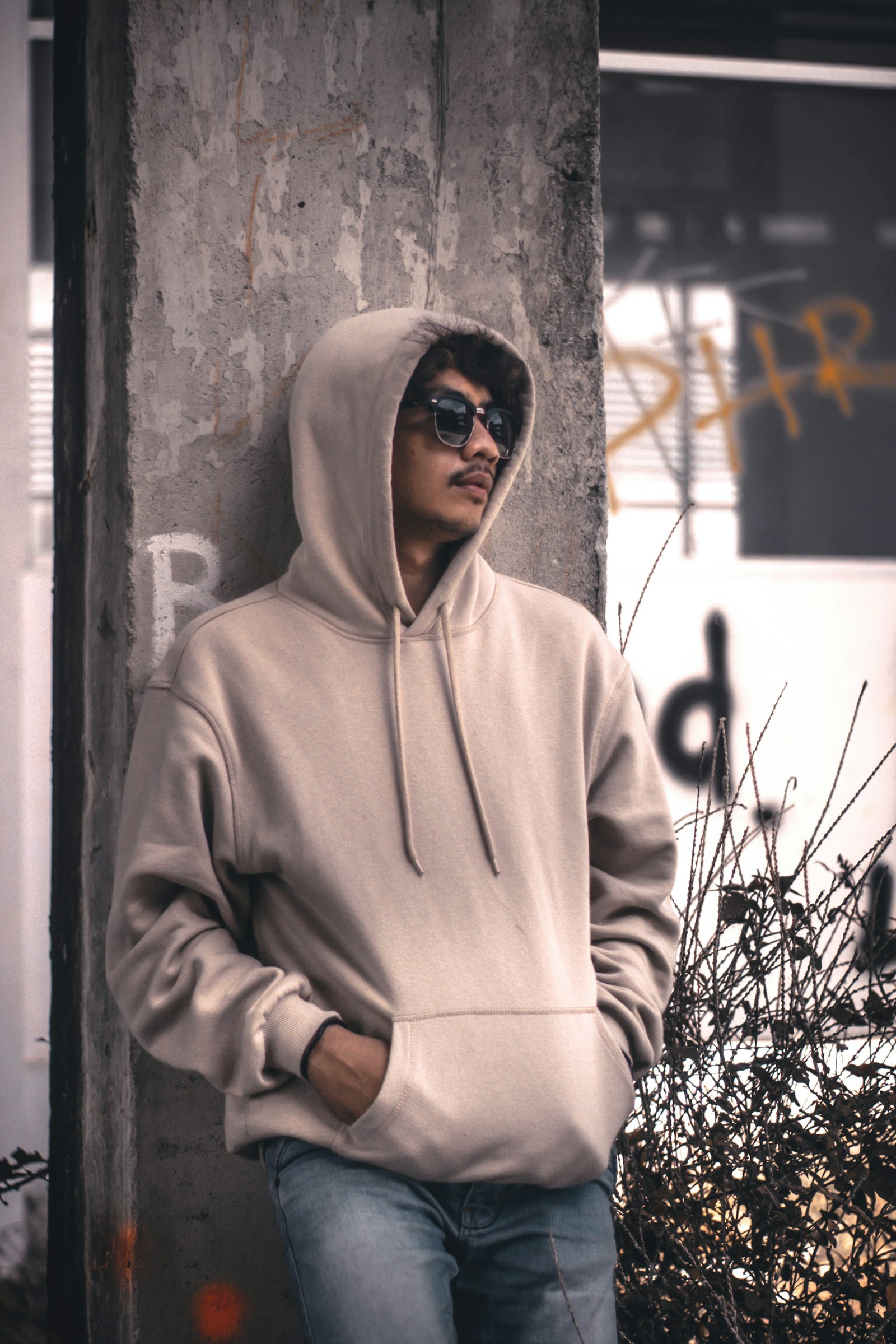 A person in a pale branded hoodie leaning against a wall outdoors
