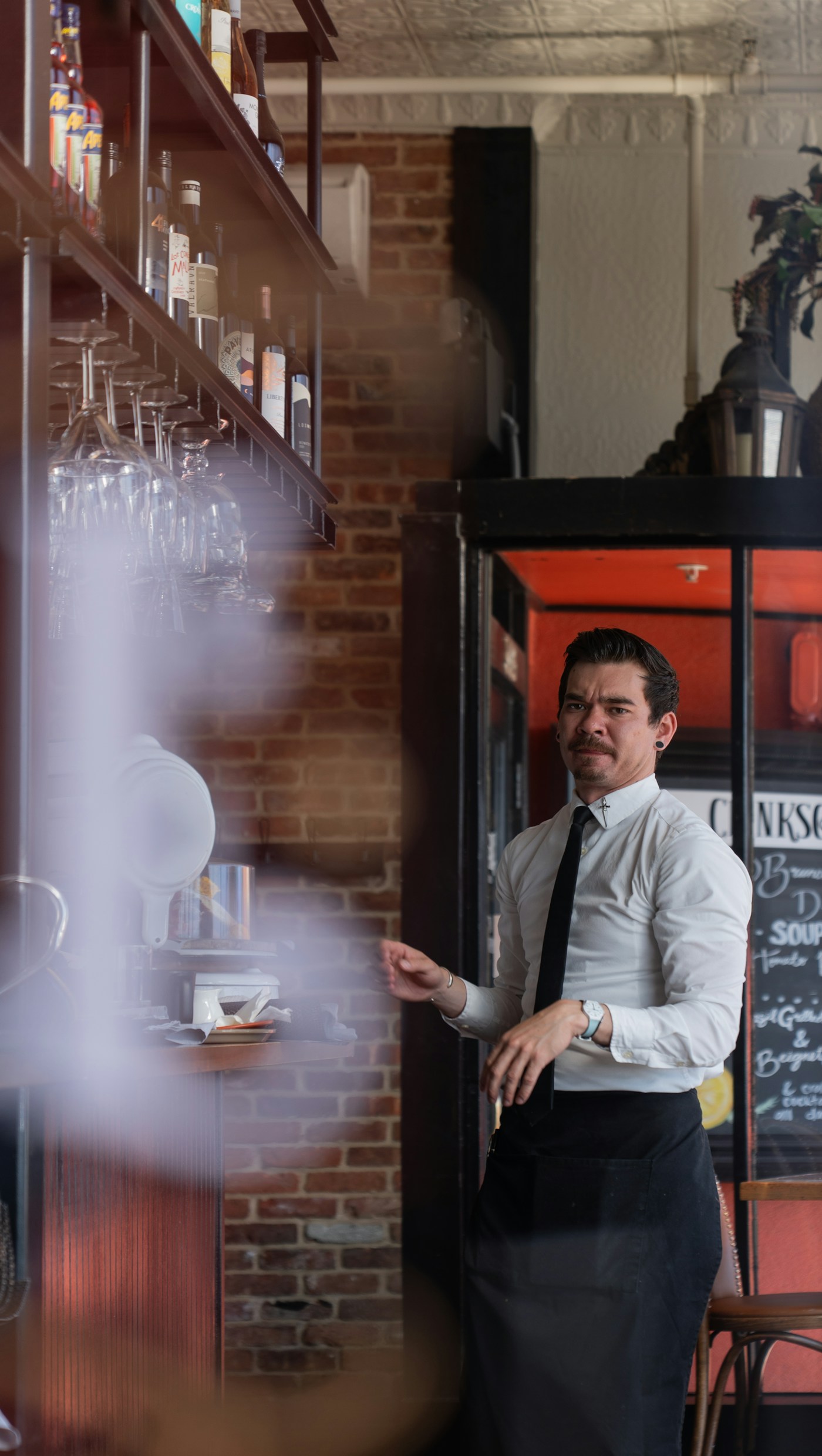 A restaurant server in a white shirt and black apron behind the bar