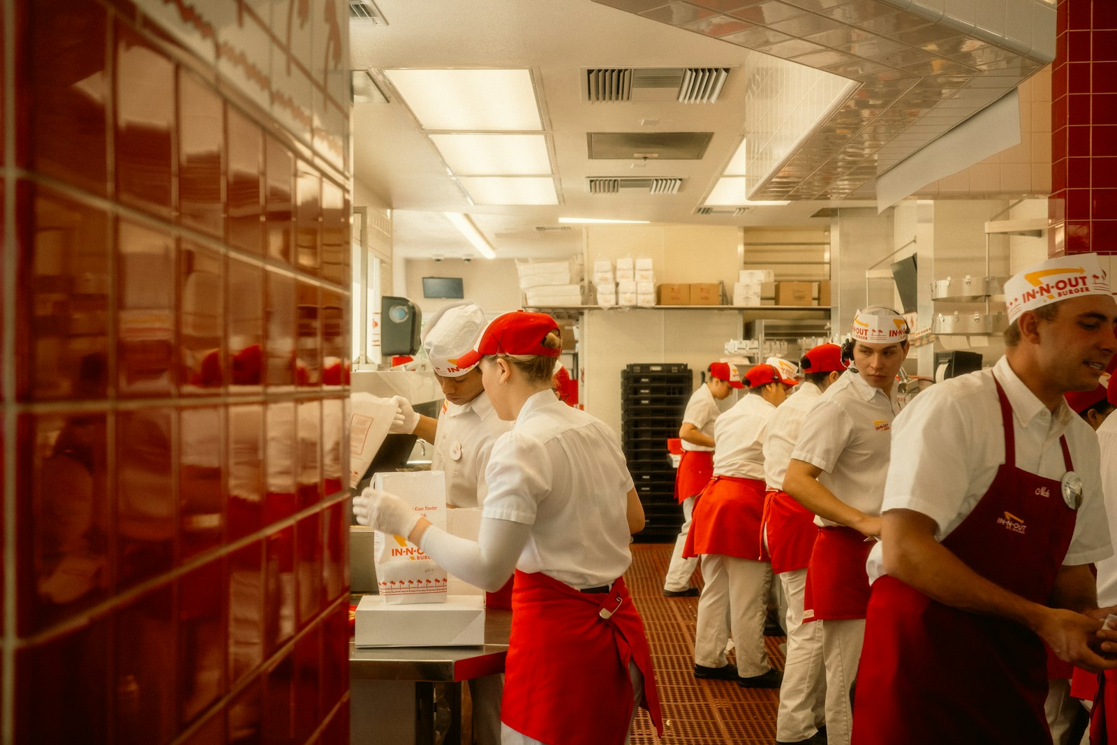 Kitchen staff in red-and-white uniforms working a busy stainless-steel line in a restaurant kitchen