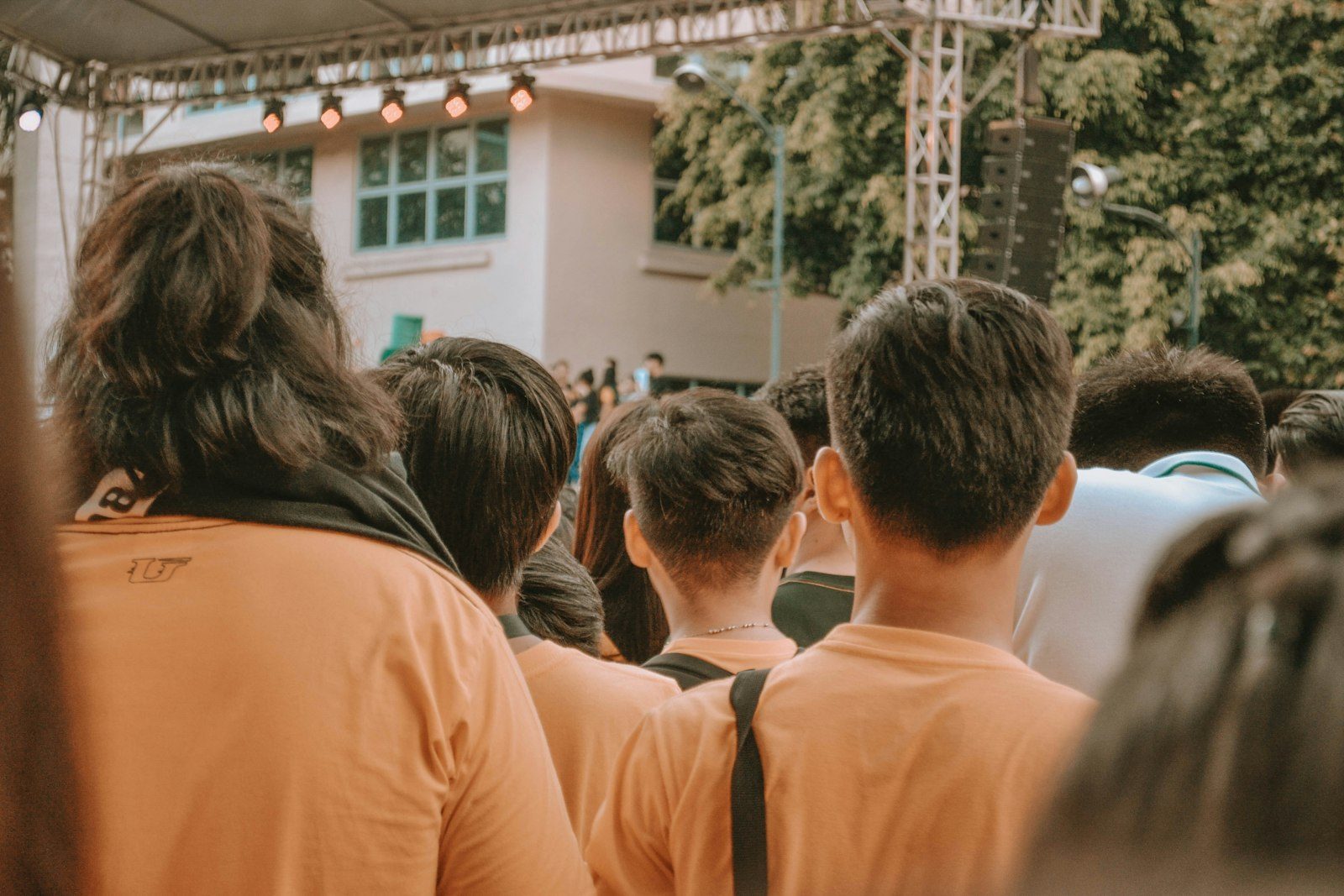 A crowd of students seen from behind, all in the same orange t-shirt, facing an outdoor stage