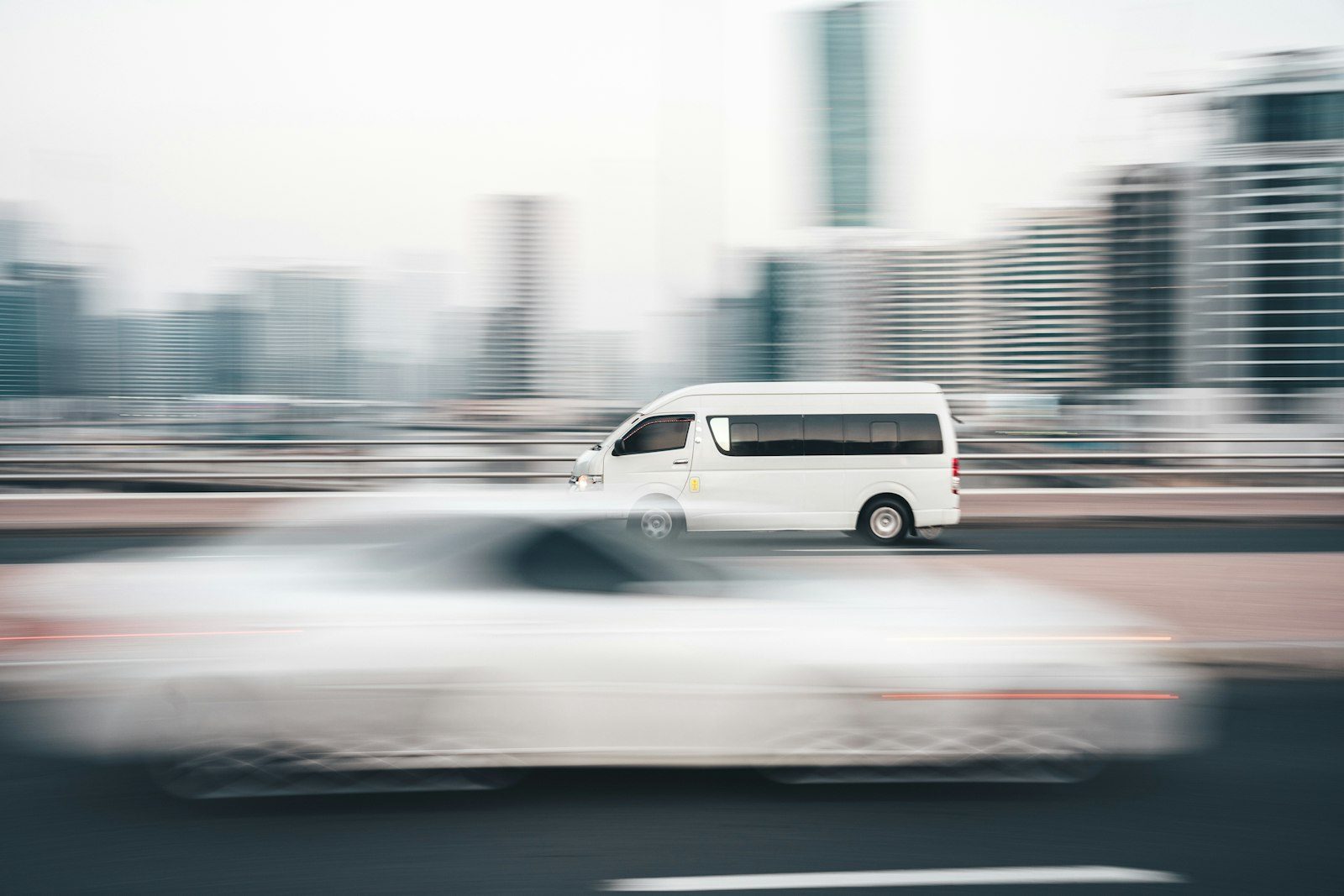 A white delivery van moving along a city road, motion-blurred against a row of office towers