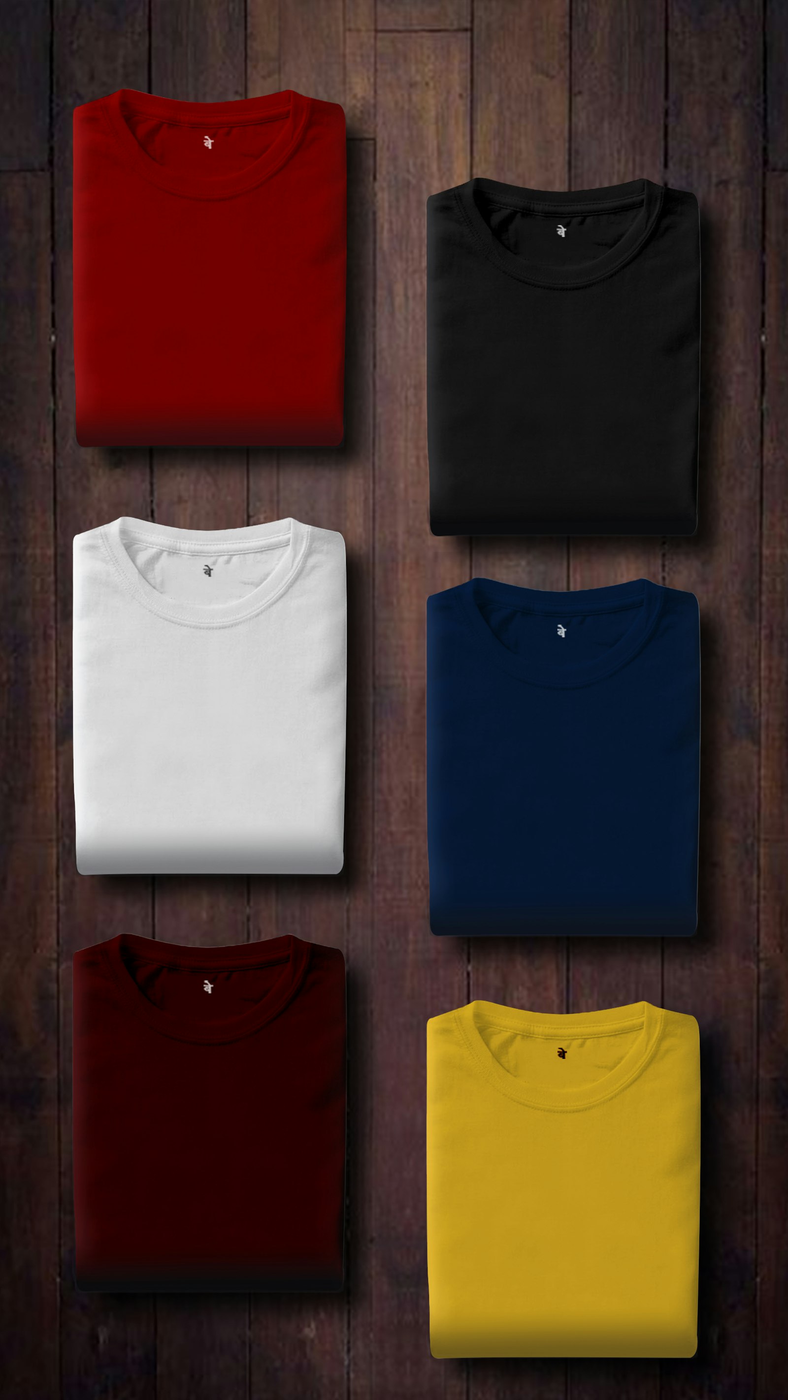 Folded blank t-shirts in red, black, white, navy and yellow laid out on a dark wooden surface