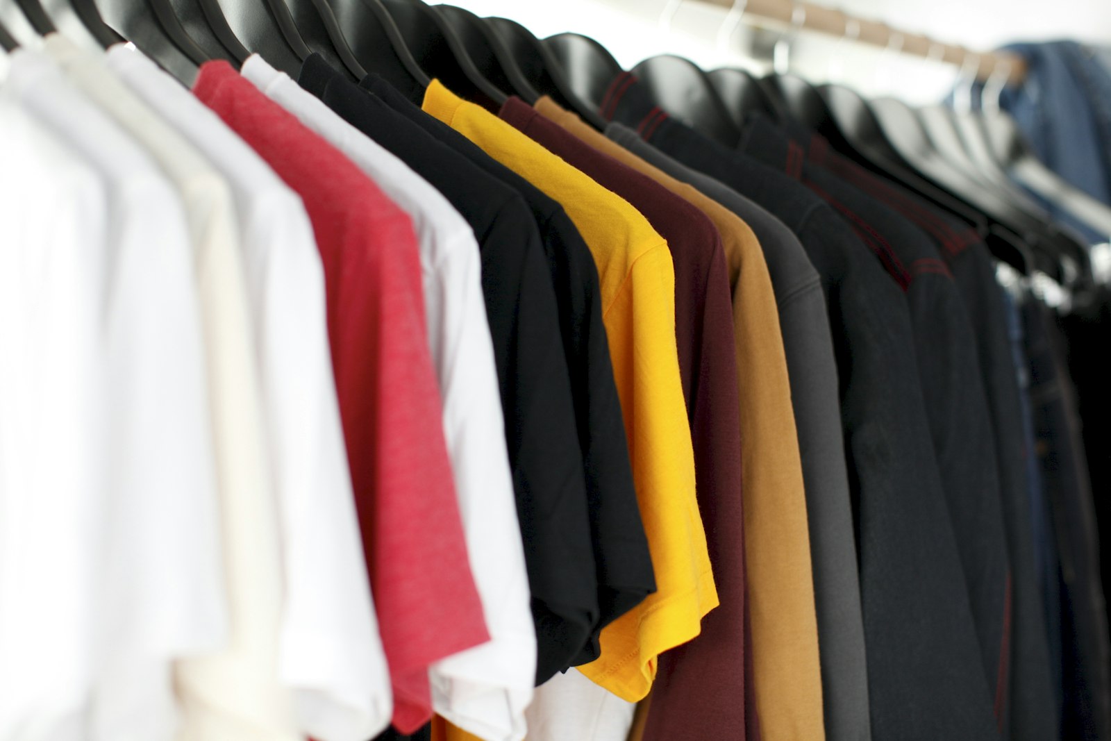 A rack of undecorated blank t-shirts on hangers in assorted colours waiting to be decorated