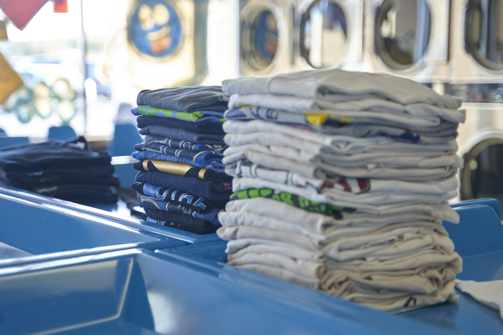 A tall stack of folded printed t-shirts in several colours sitting on a shop table after a bulk run