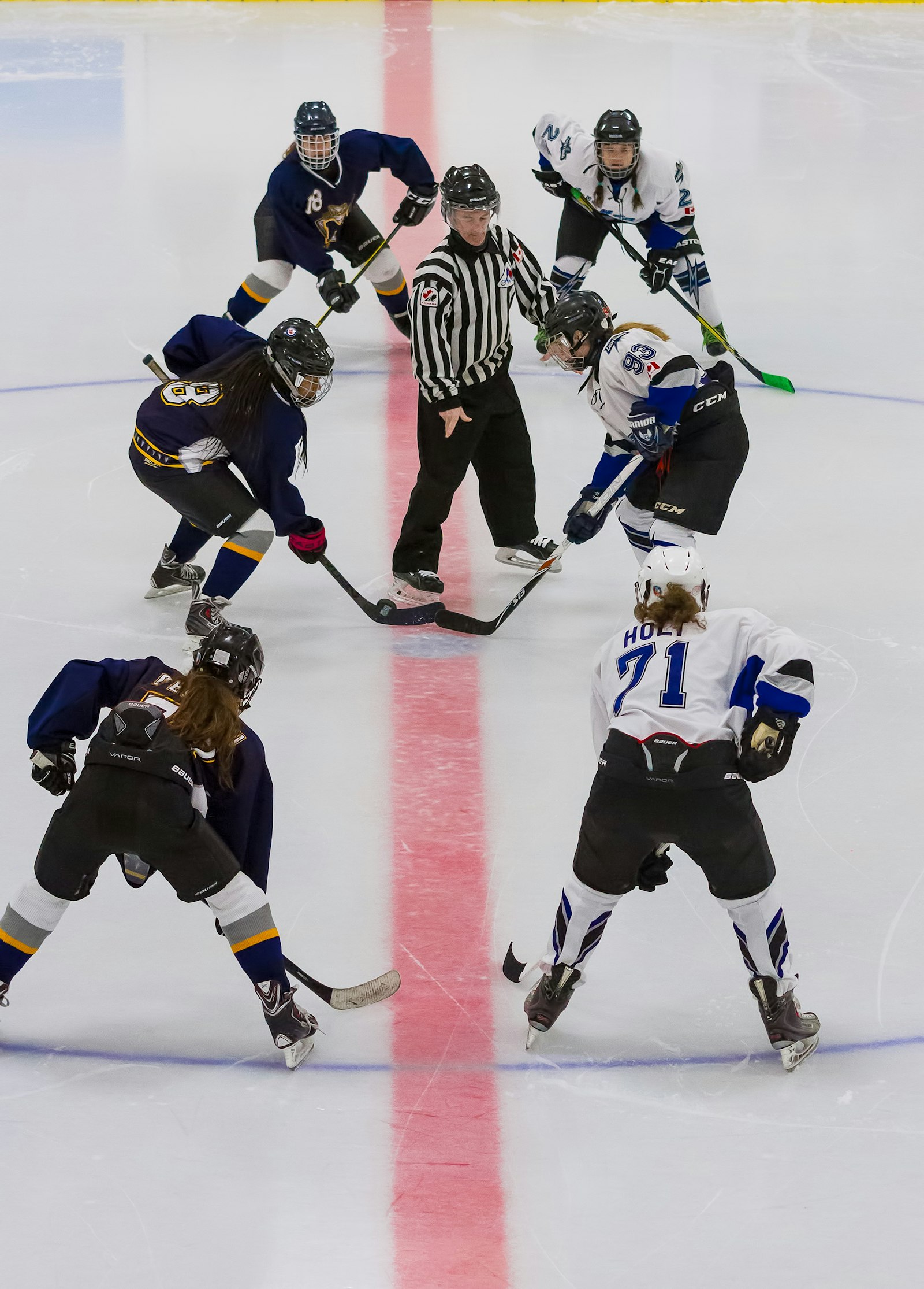 Young hockey players in dark and white jerseys at a face-off in front of a referee on an indoor rink