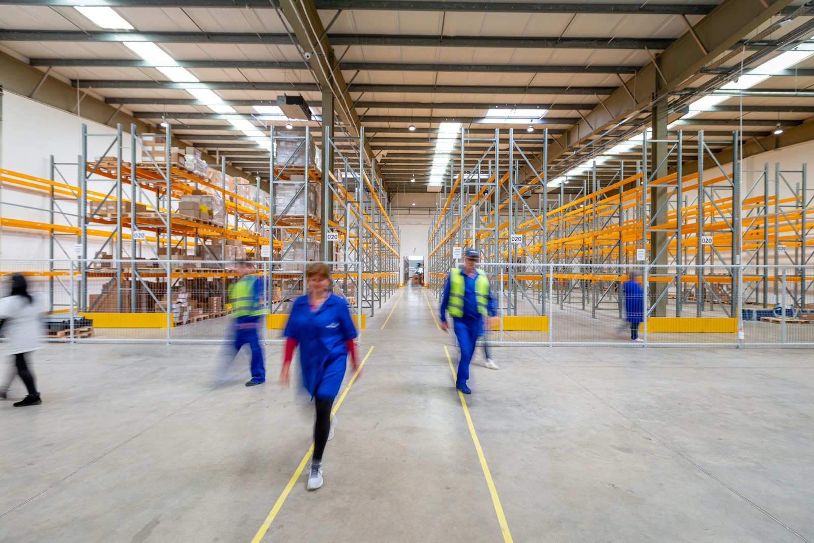 A bright distribution warehouse with orange racking and workers in blue walking the main aisle