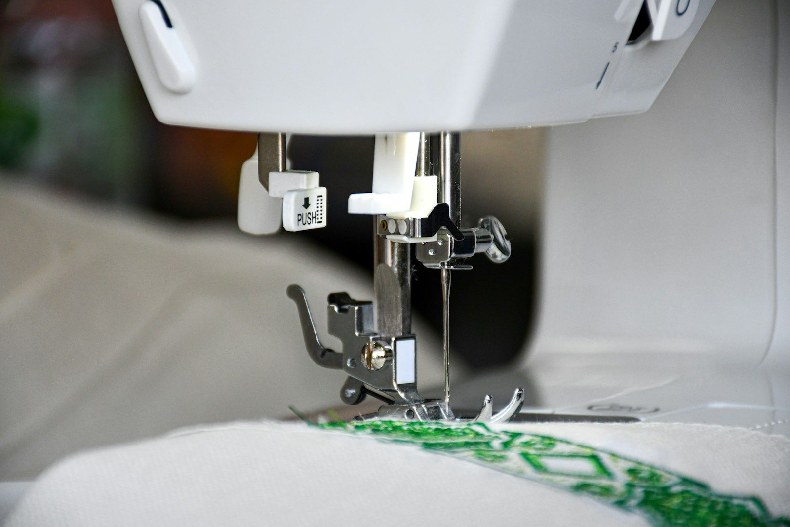 The needle head of an embroidery machine stitching a green and white design into white fabric