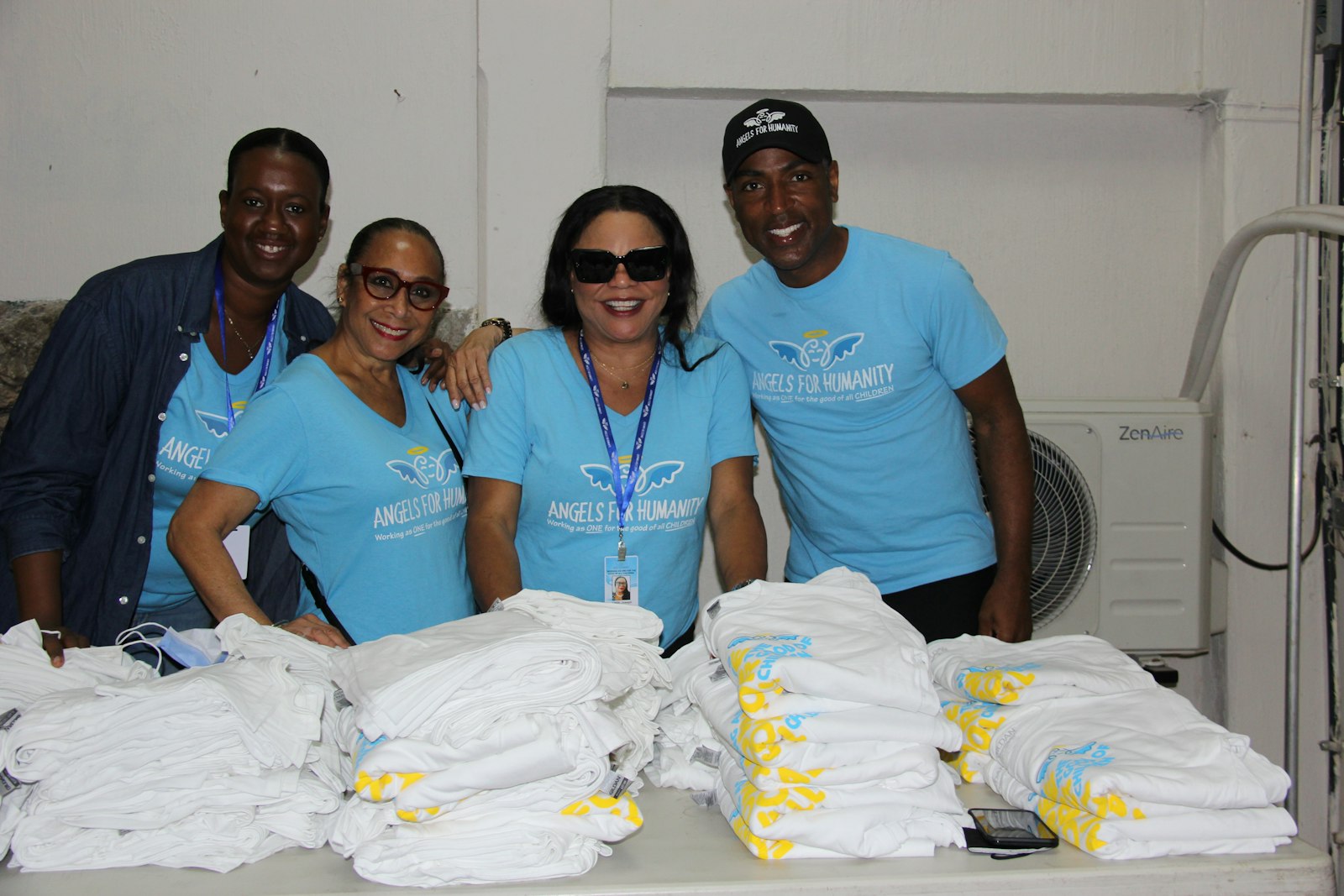 Four volunteers in matching light-blue printed t-shirts standing behind a table stacked with folded white shirts