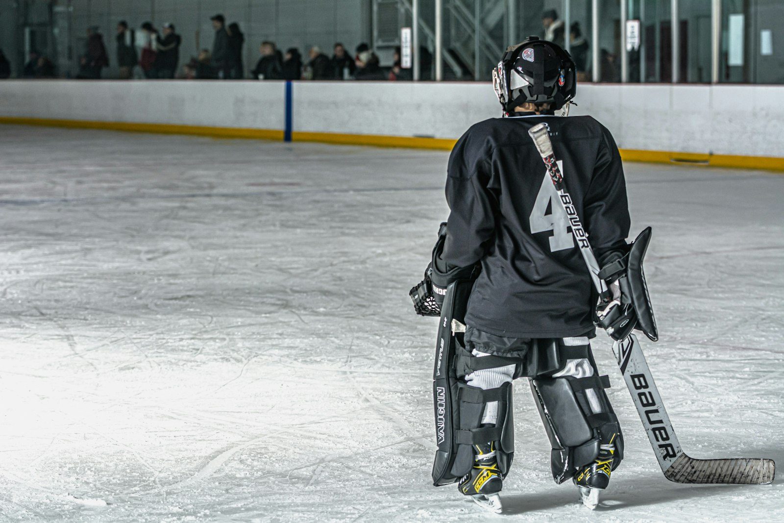 A young goalie in a black jersey with the number 4 on the back skating across a community rink