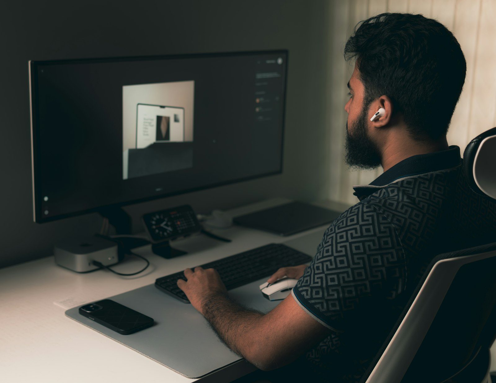 A designer seated at a desk, seen from behind, working on an image open on a large monitor