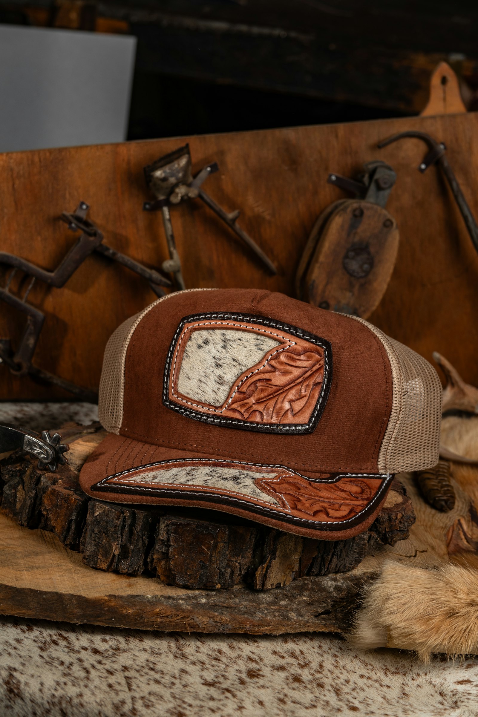A brown trucker cap with a tooled leather patch resting among leather tack and hide