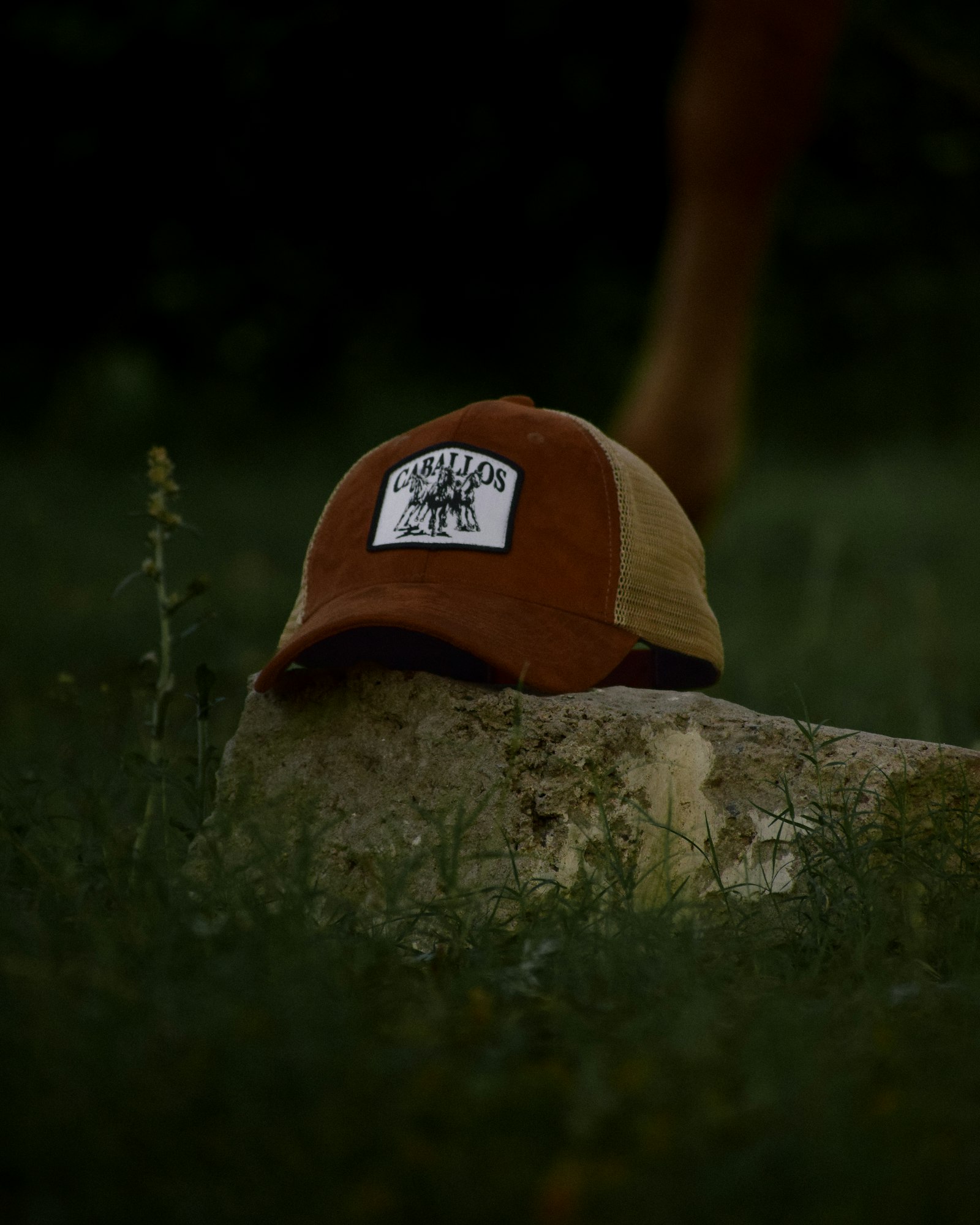 Close view of a leather patch stitched to the front of a brown trucker cap resting on stone