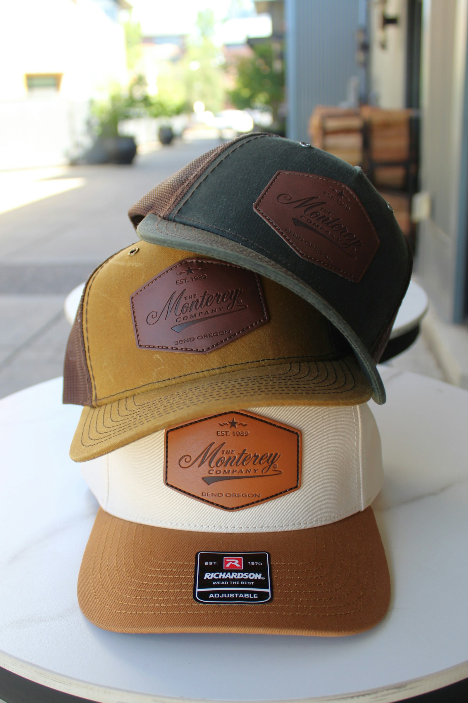 Three two-tone trucker caps with front patches stacked on white café tables