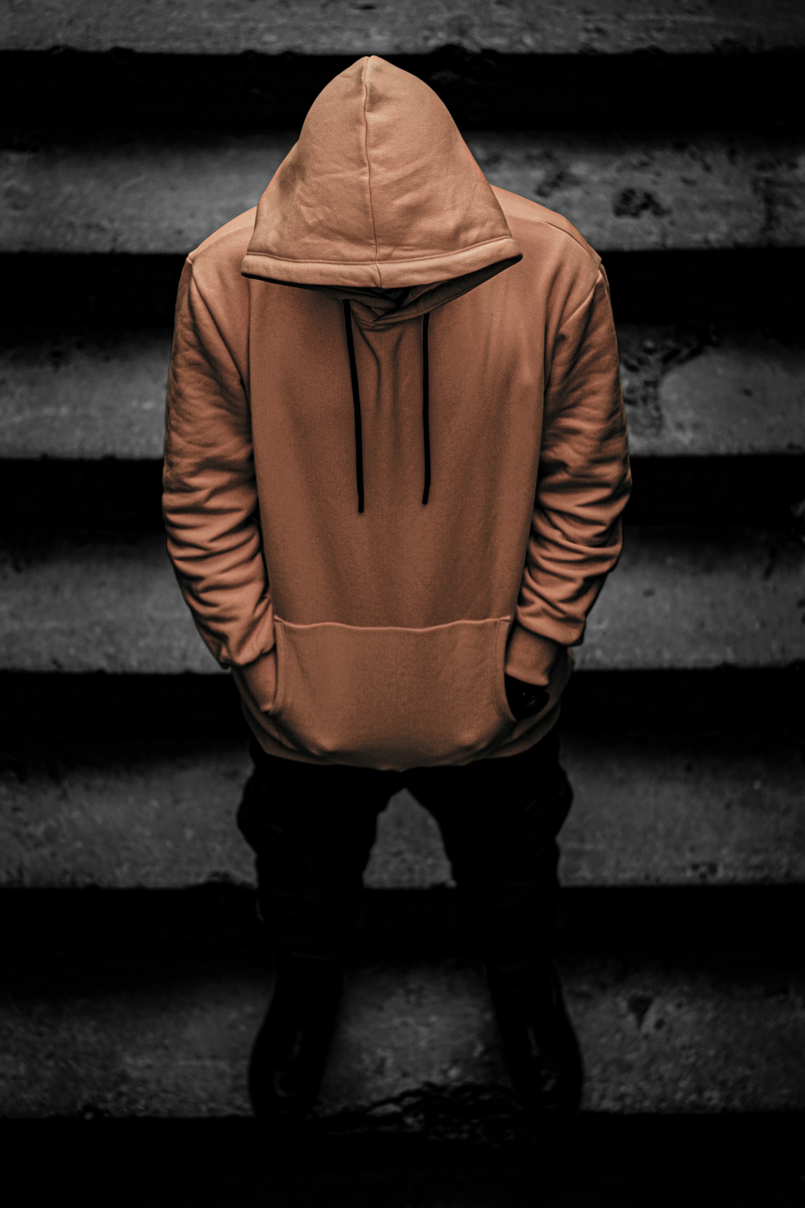 A person in a brown hoodie and black trousers standing on a concrete staircase