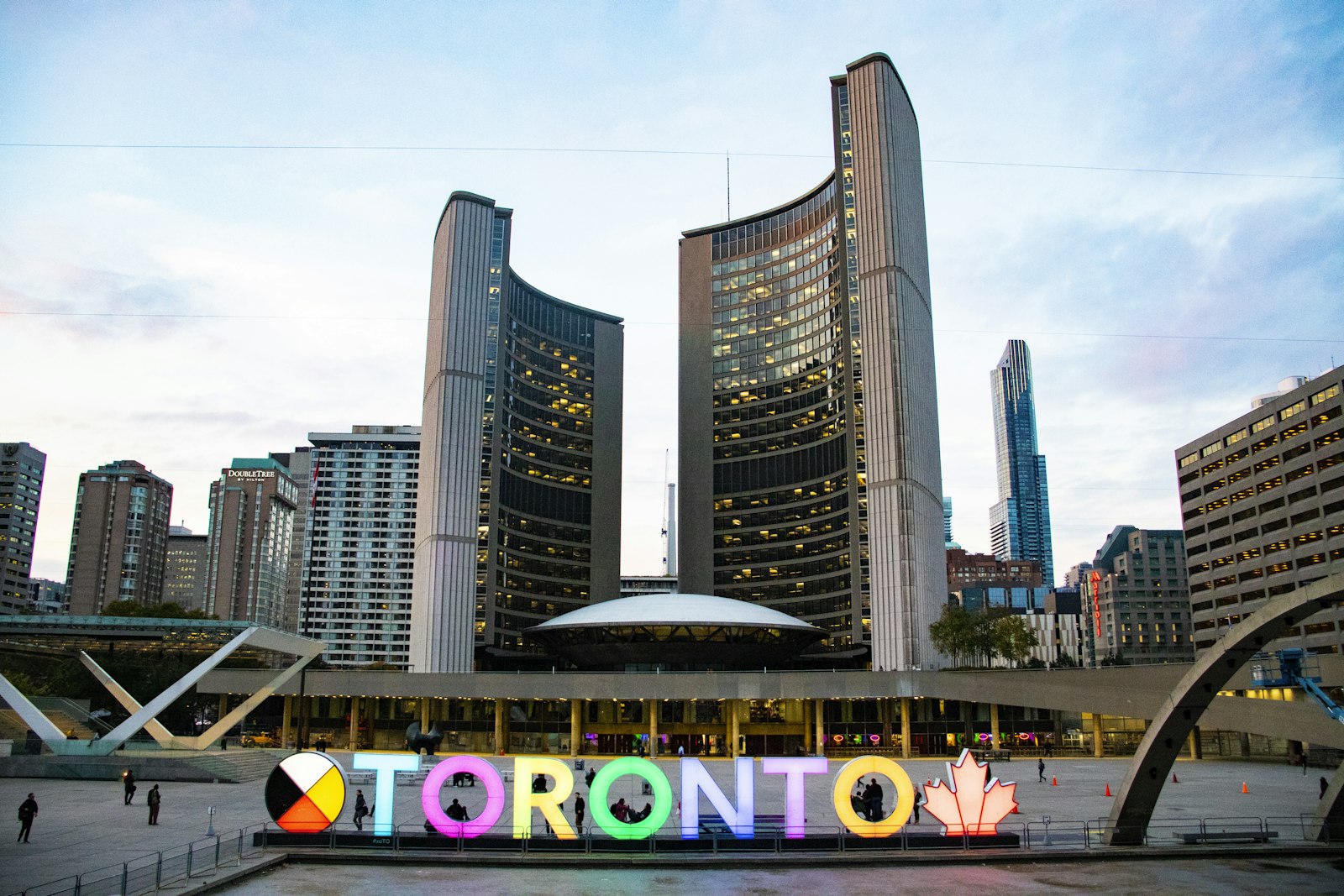 Toronto City Hall's curved twin towers and the multicoloured 3D TORONTO sign at Nathan Phillips Square on an overcast day