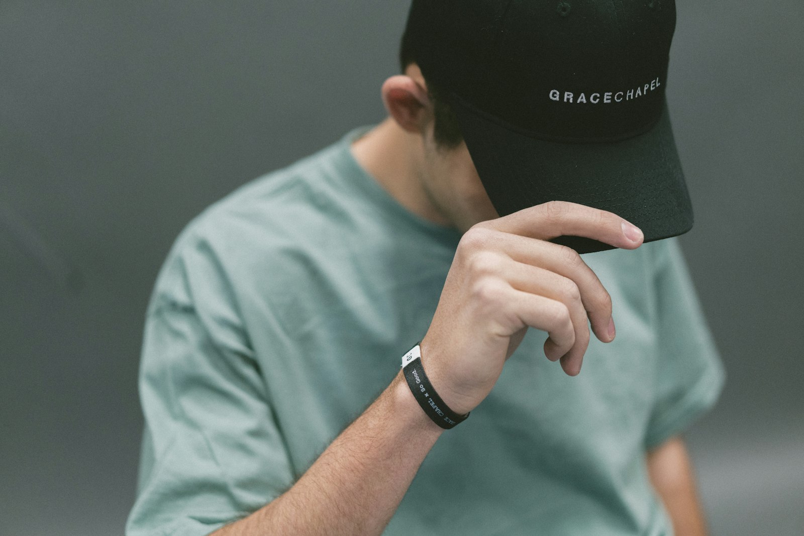 A person in a pale green t-shirt wearing a dark cap with small embroidered lettering