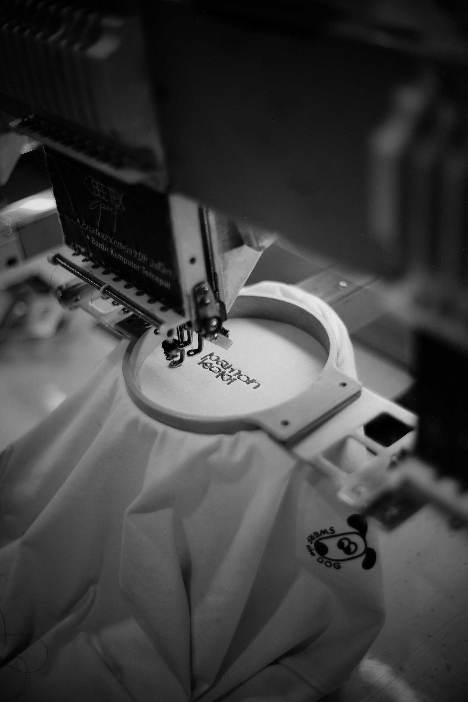 An industrial multi-needle embroidery machine stitching a design into white fabric