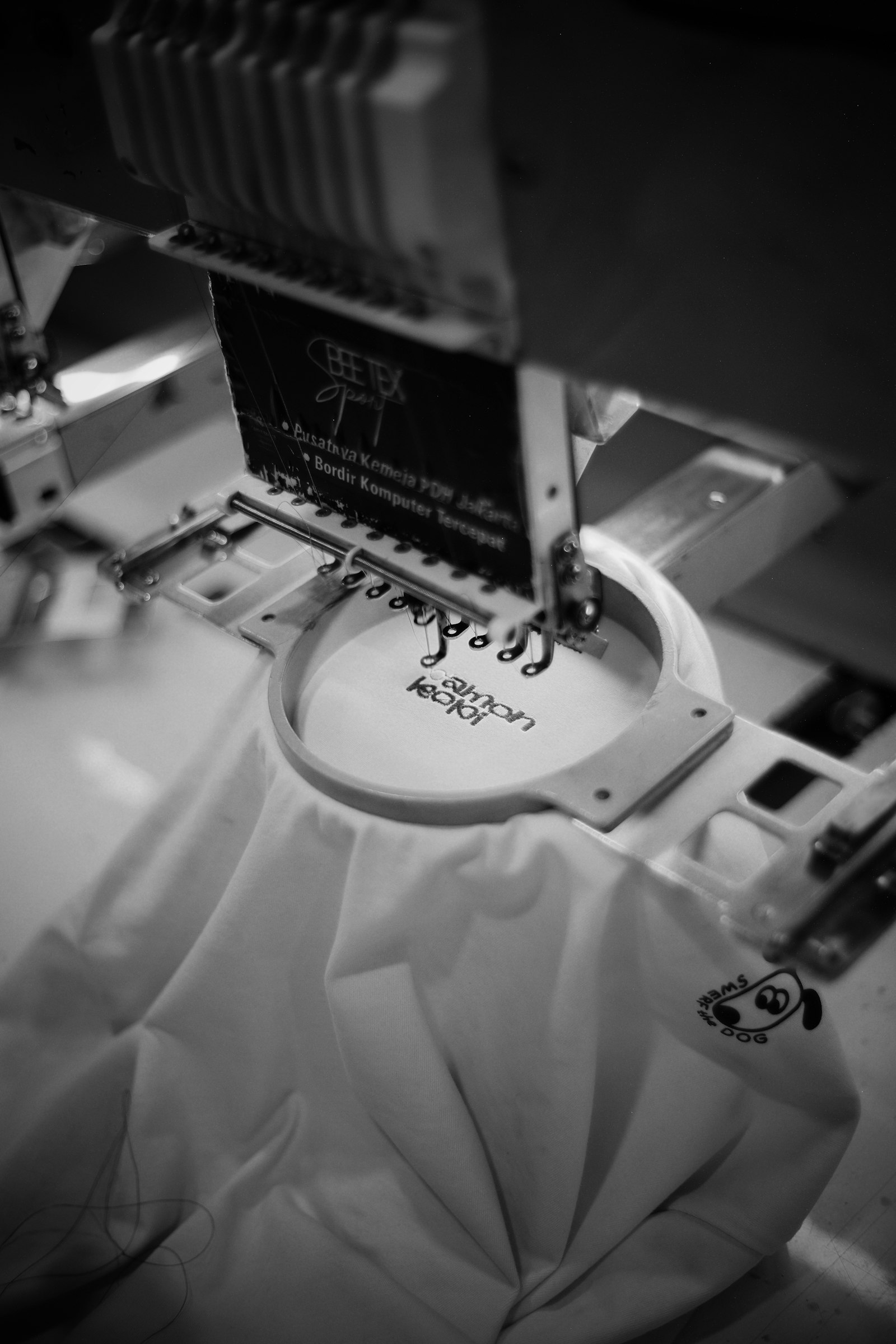 An embroidery machine head stitching a logo into white fabric in close view