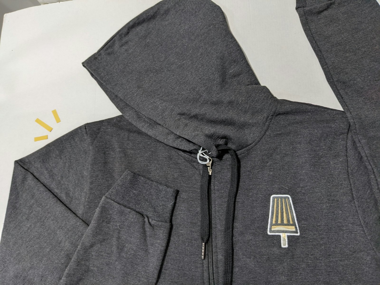 A folded dark grey zip-front hooded sweatshirt with a small embroidered chest motif