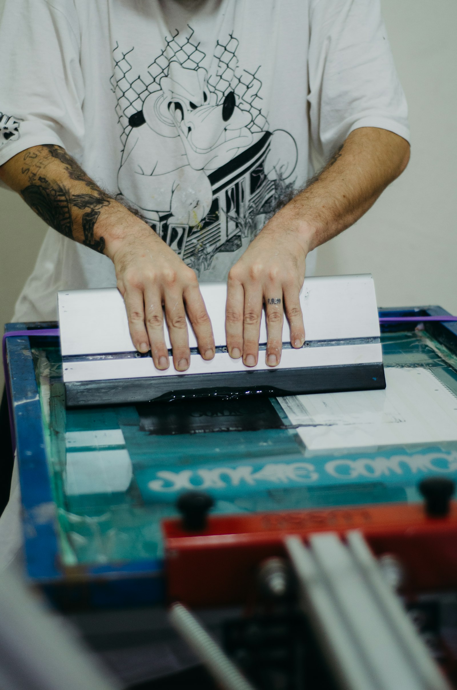 A printer working a screen on a press with a printed graphic visible on the platen below