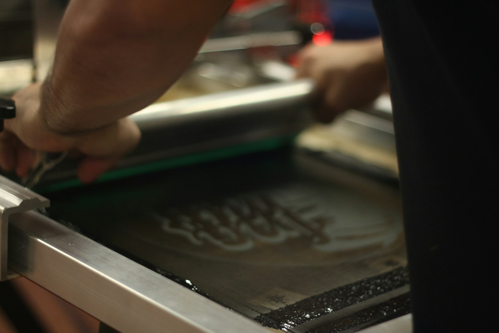 Hands drawing a squeegee across a screen with the design visible through the mesh