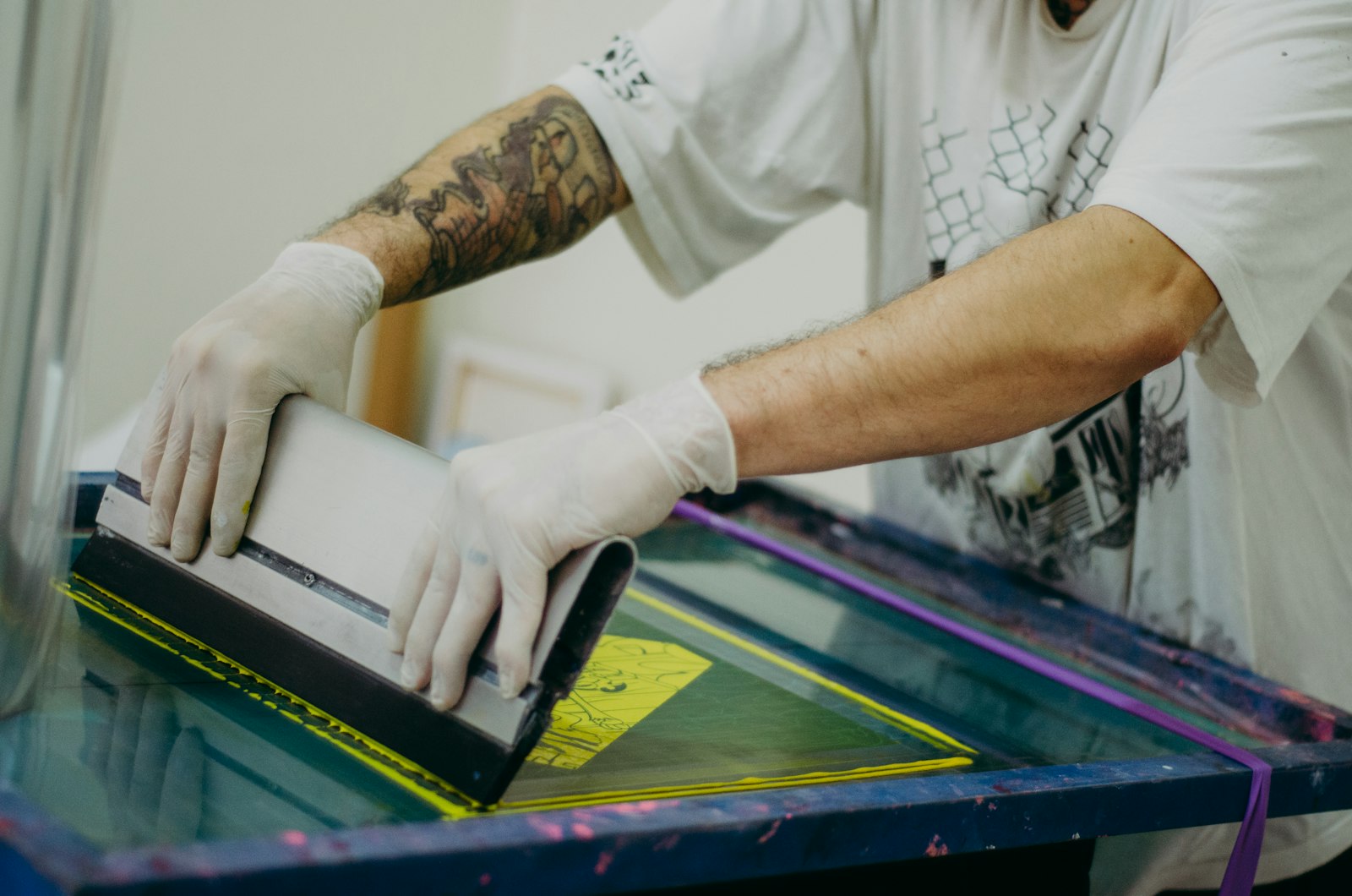 Gloved hands drawing a squeegee across a screen on a printing press
