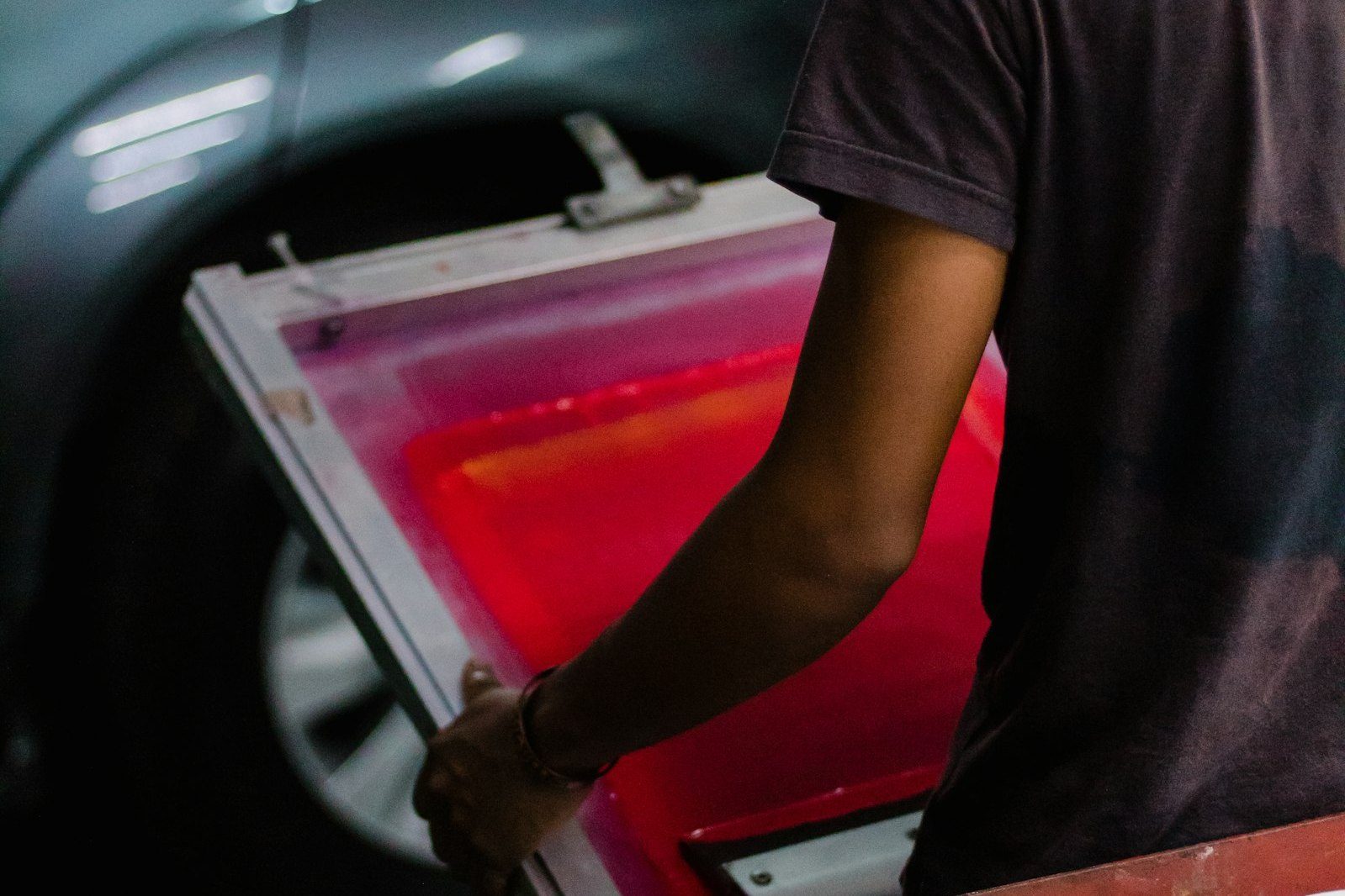 A printer carrying a screen-printing frame, pink and red ink visible in the mesh