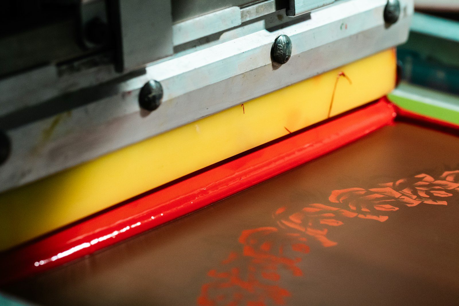 Close-up of a squeegee drawing red ink across a mesh screen on a press
