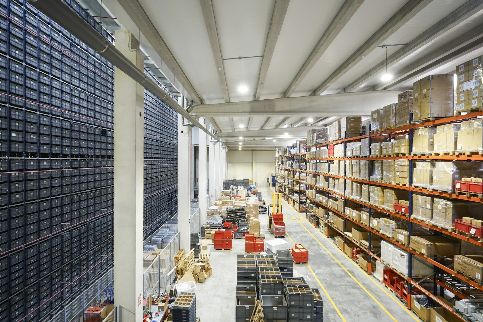 A long, brightly lit warehouse with tall racks of cartons and rows of stacked bins