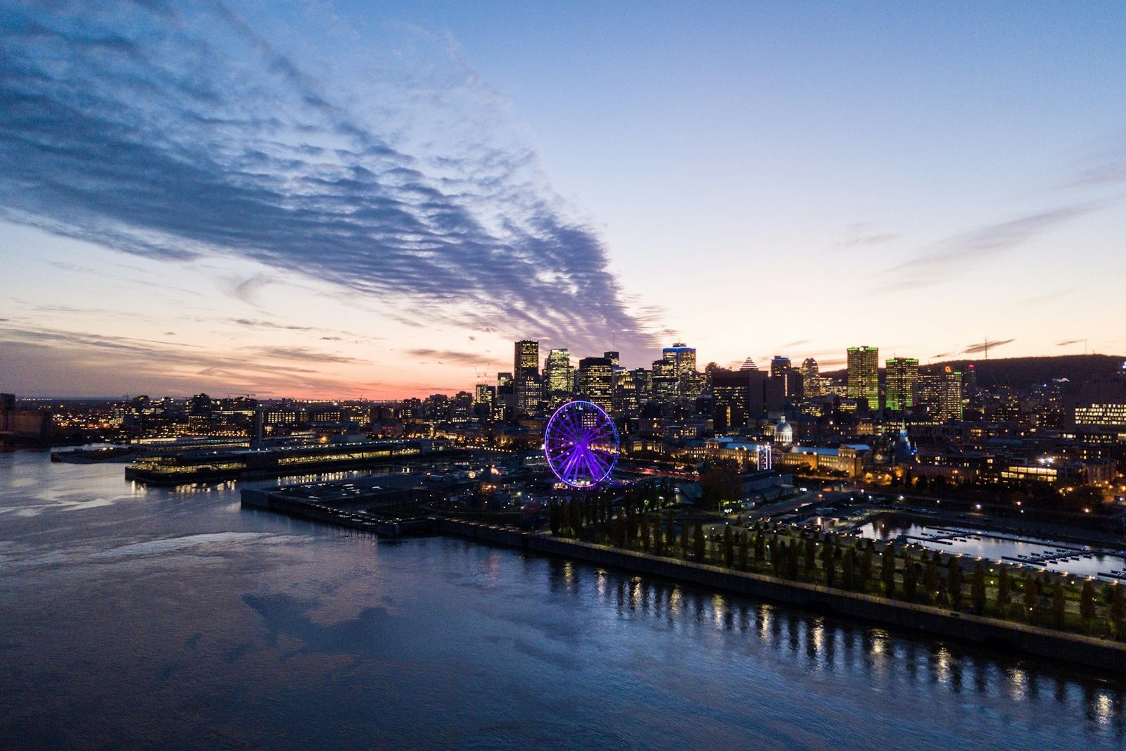 Montreal’s Old Port and downtown skyline at dusk, the Ferris wheel lit purple beside the river