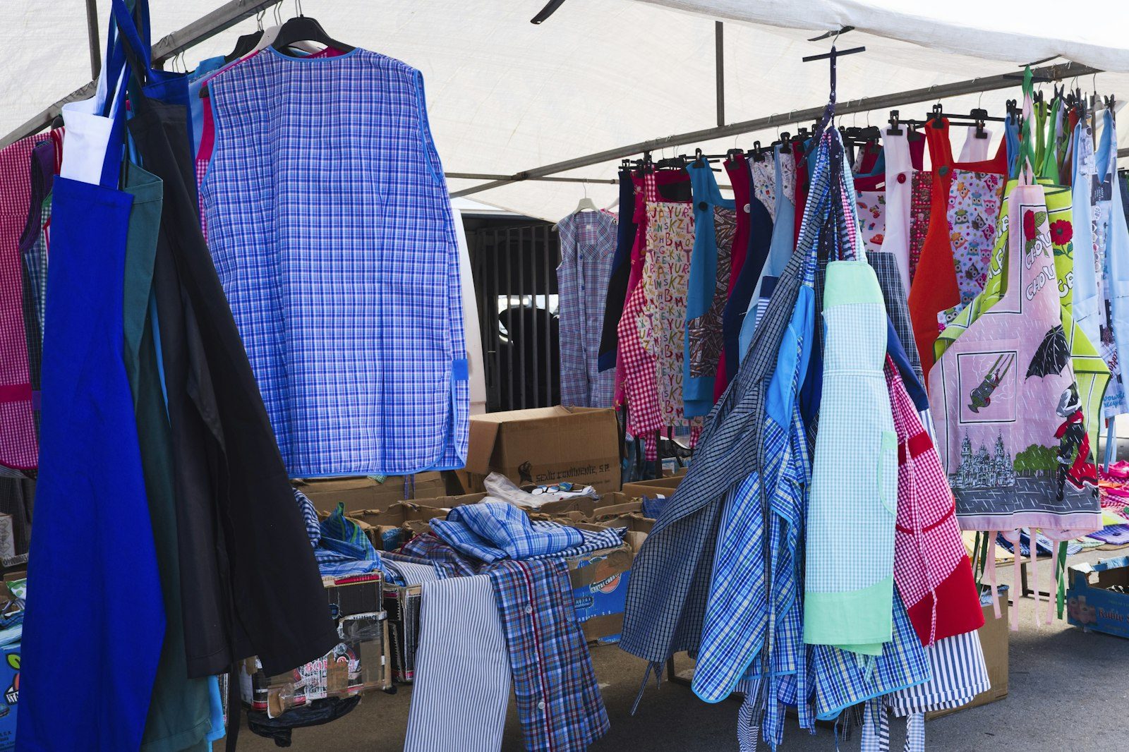 Racks of shirts and dresses hanging under a white canopy at an outdoor market stall