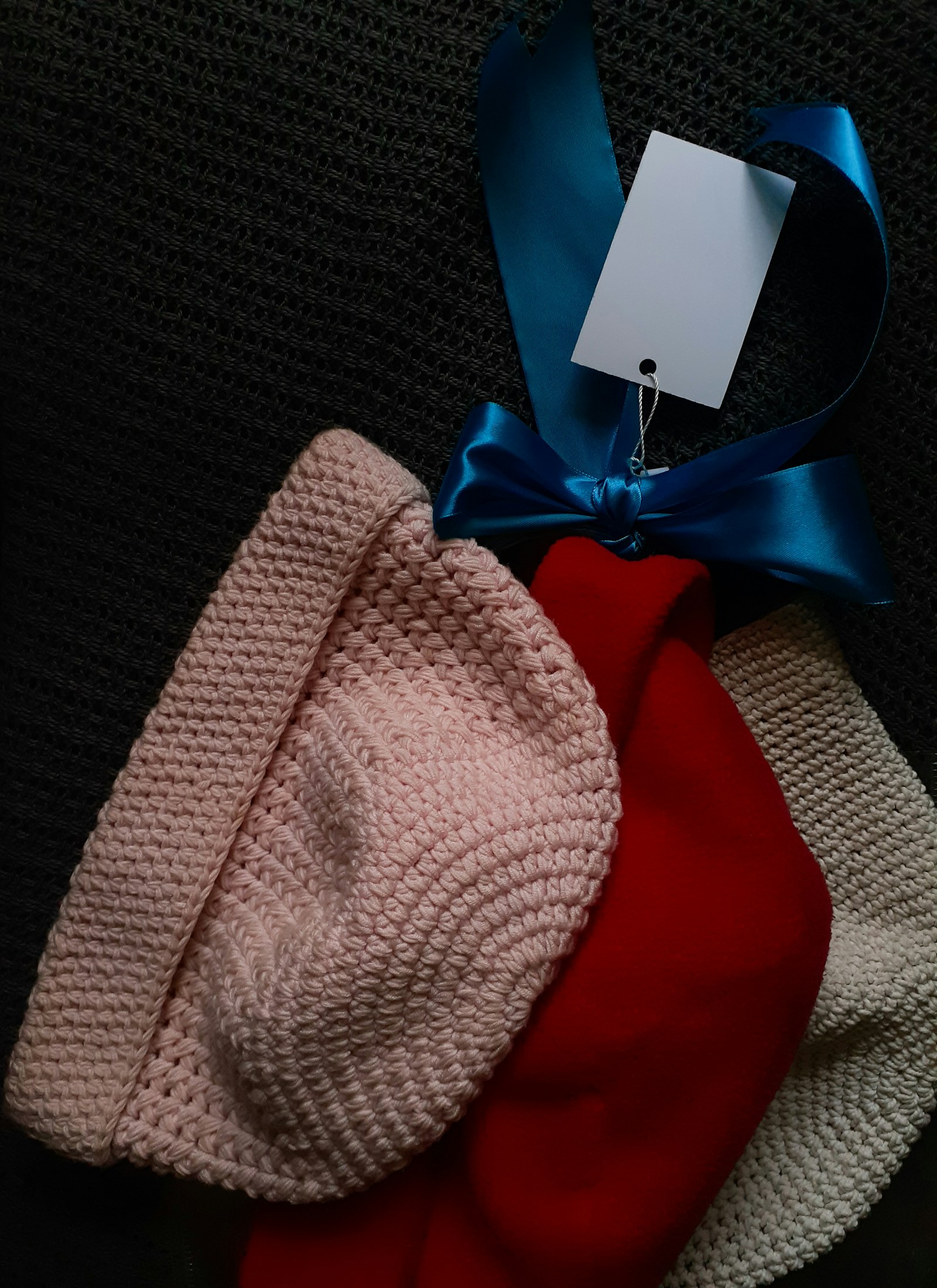 Three knitted toques in pink, cream and red stacked together with a tag attached